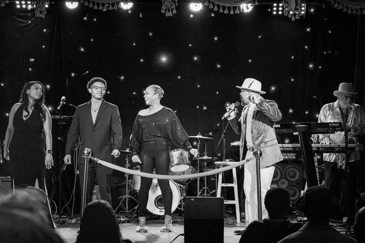 Black and white photo of band performing on stage with theatrical lighting and decorative elements.