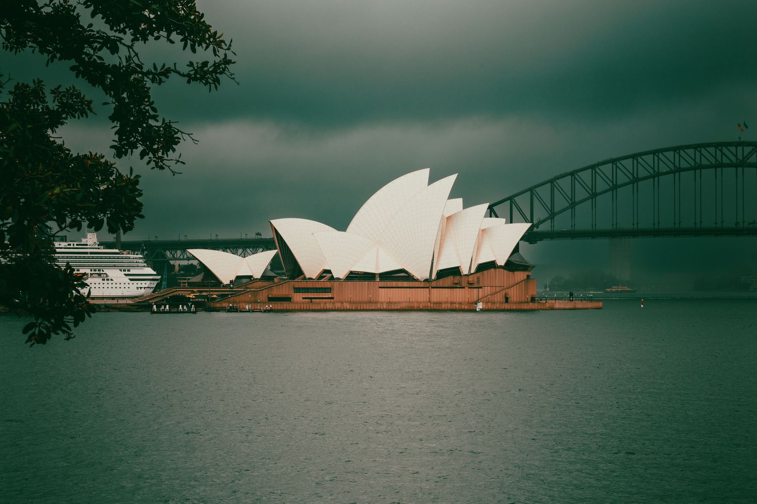 Sydney Opera House and Harbour Bridge silhouetted against moody green-tinted sky.