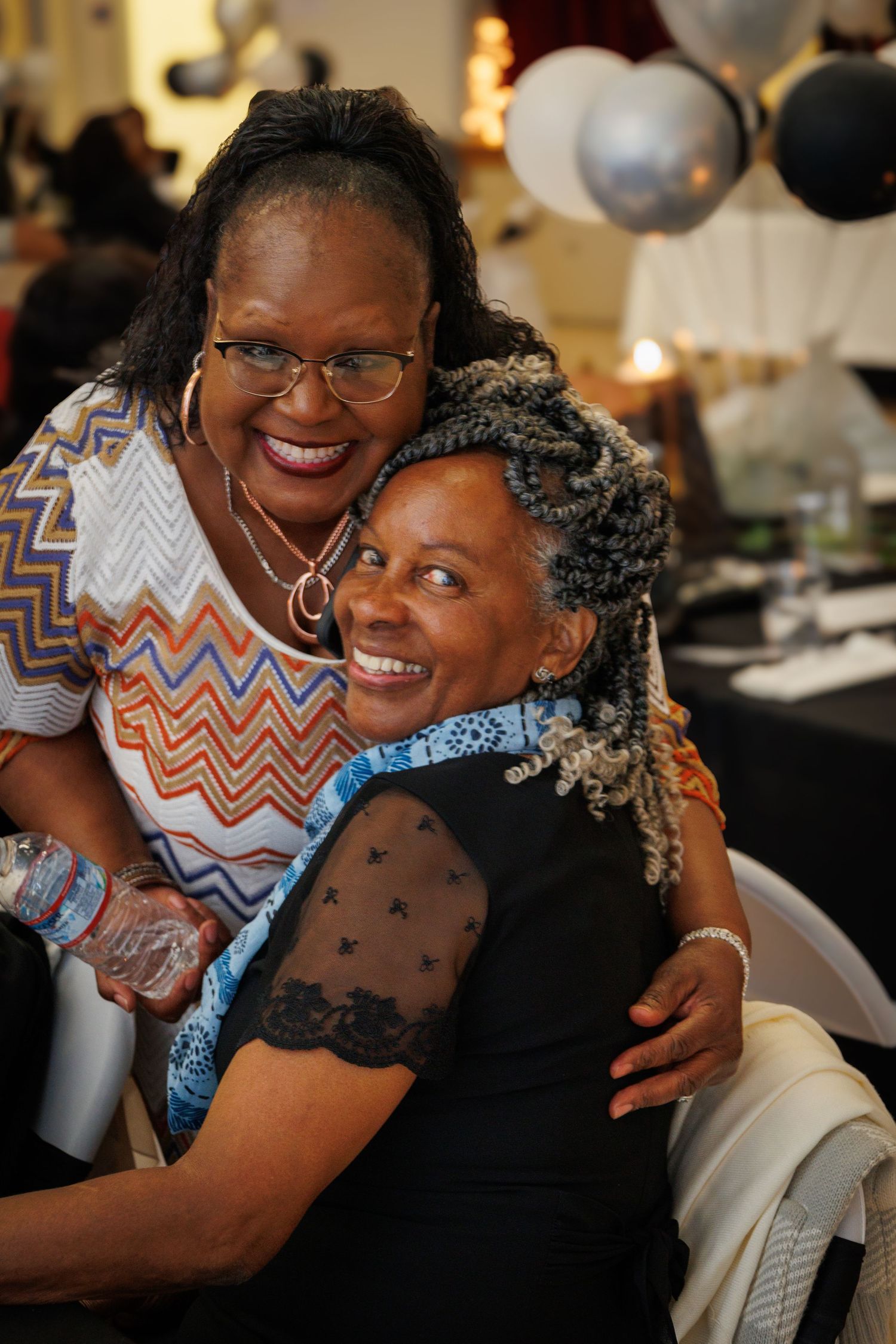 Warm embrace shared between two people wearing glasses at a social gathering.