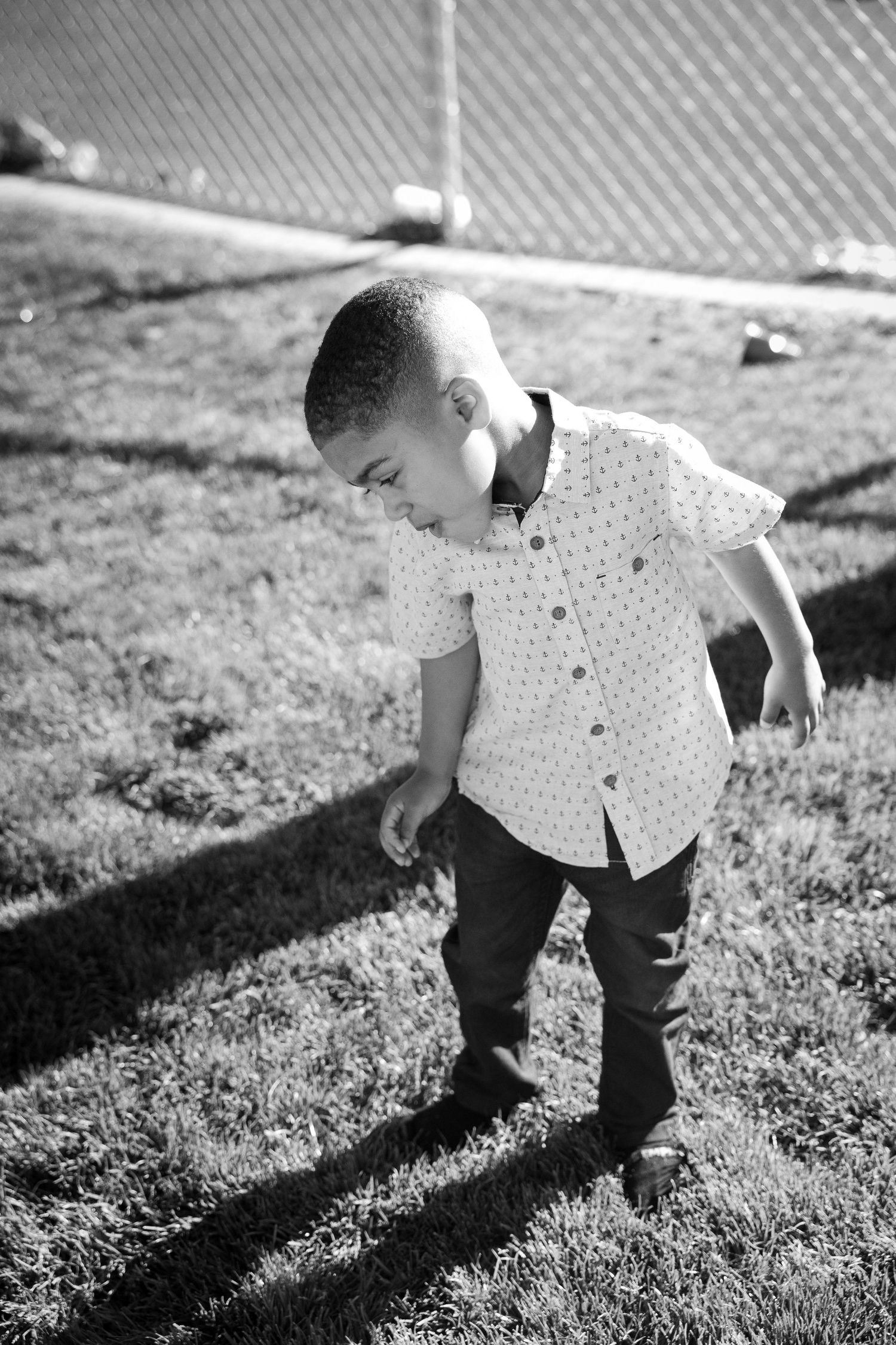 Black and white portrait of young child exploring grassy area in polka dot shirt.