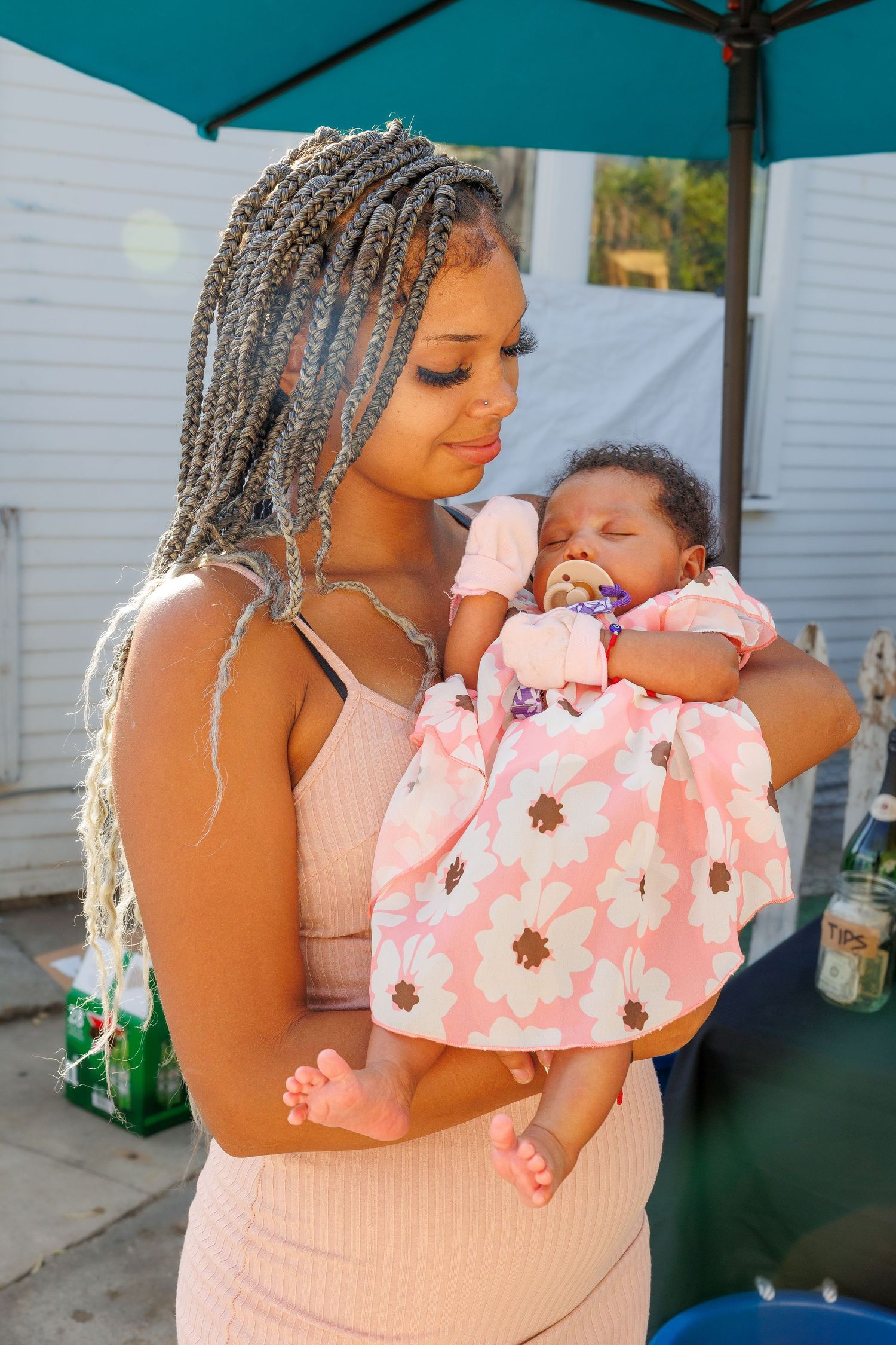 Woman in pink dress holding and comforting a baby under a teal umbrella.