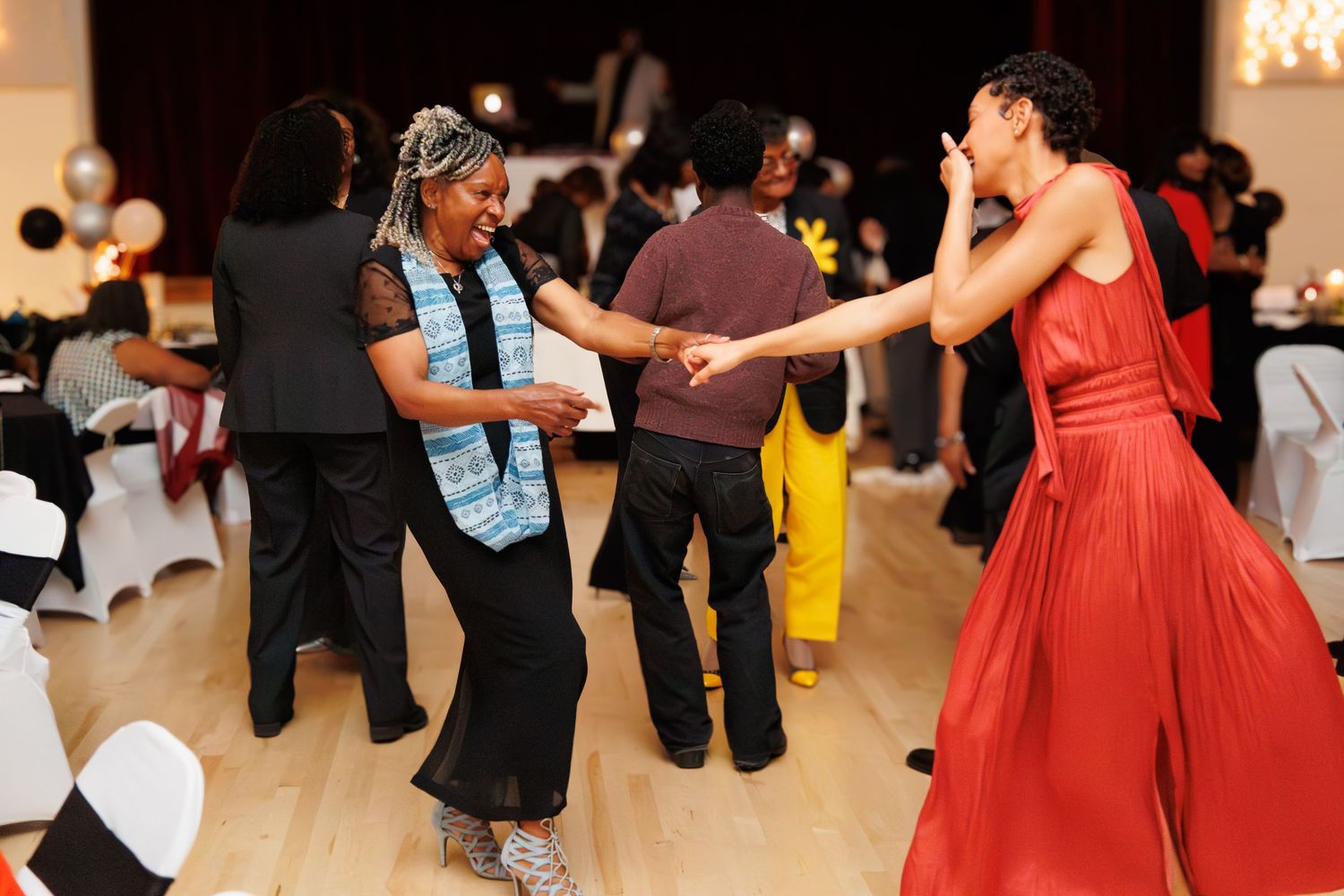 People dancing and celebrating at an indoor event with red dresses visible.