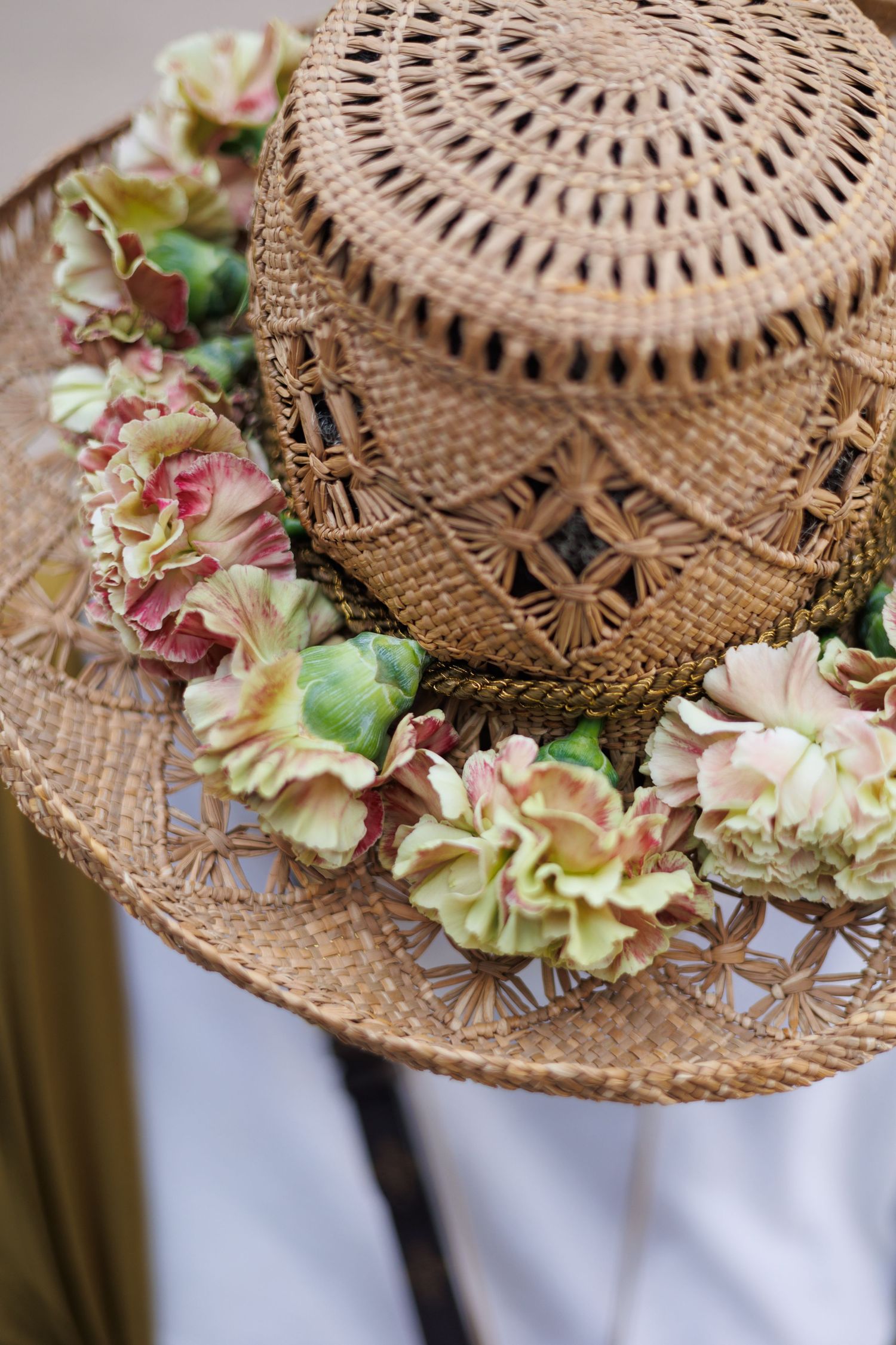 Straw hat adorned with delicate pink and green floral decorations against a white background.