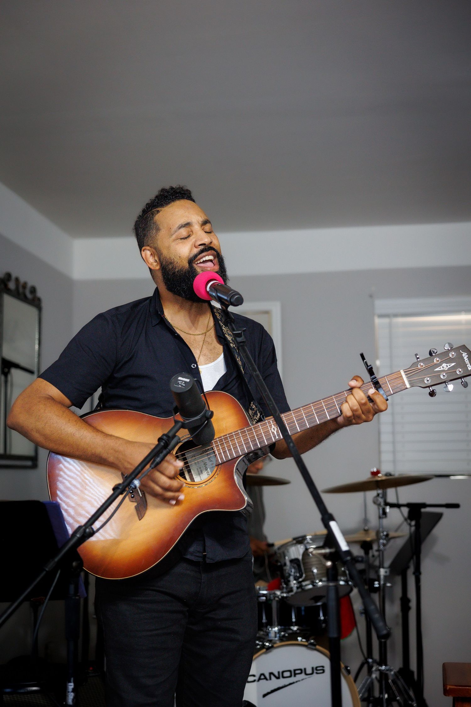 Musician performing with an acoustic guitar and microphone in a studio setting.