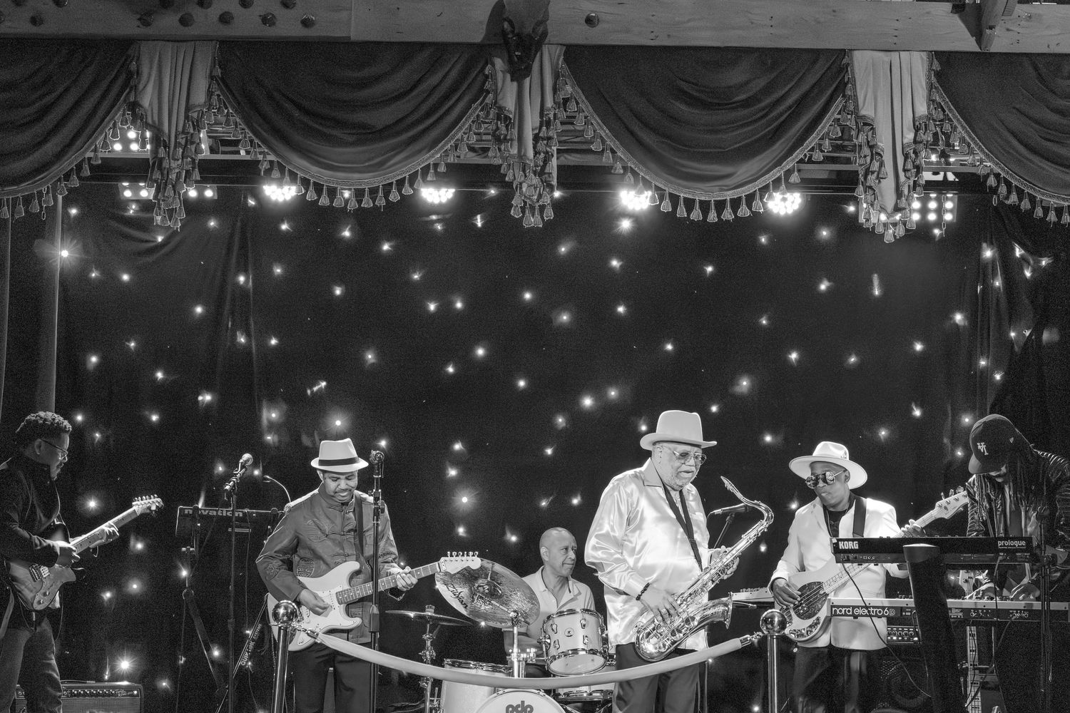Musicians perform under starlit ceiling with dramatic stage lighting and theatrical curtains.