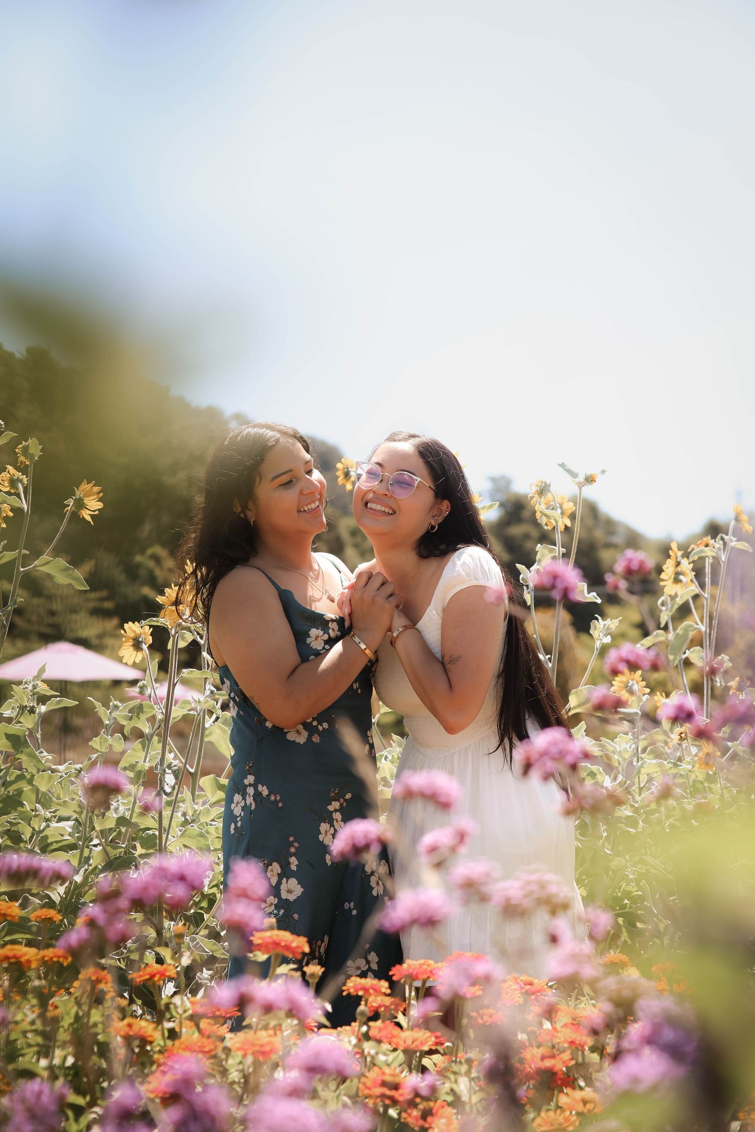 A couple share joyful laughter while sitting among colorful wildflowers in a sunny garden setting. Proposal.
