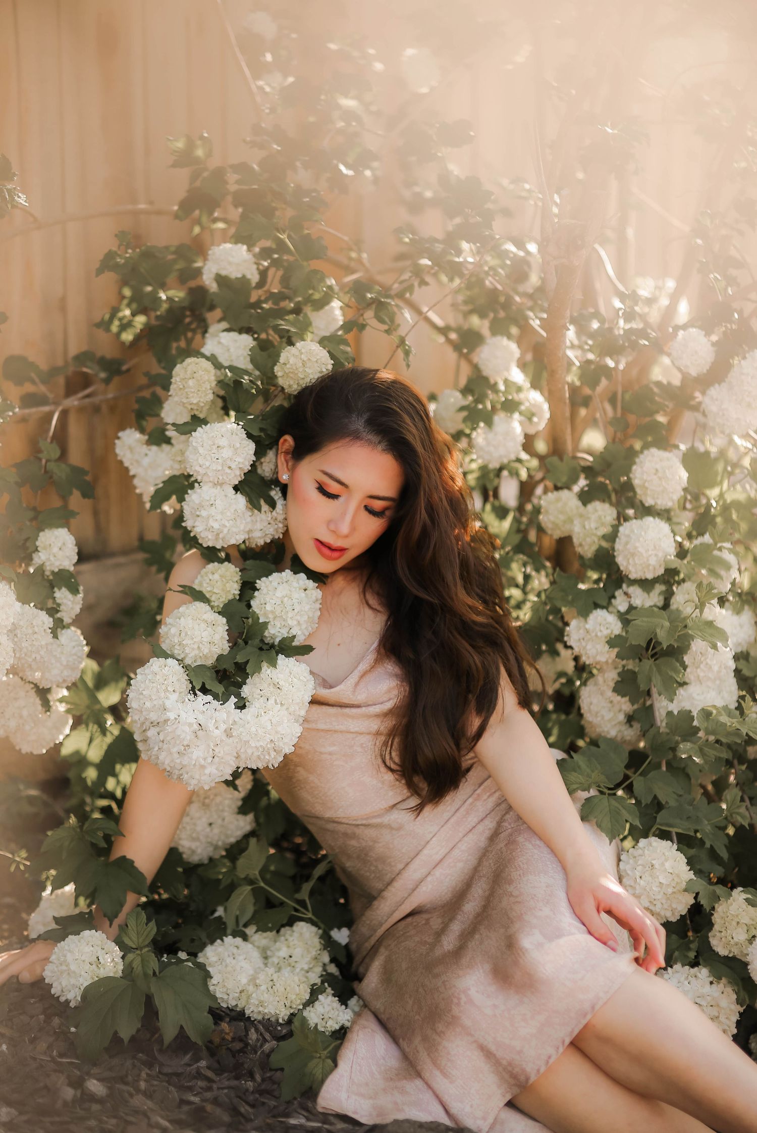Dreamy portrait surrounded by abundant white hydrangea blooms and greenery against a soft beige wall.