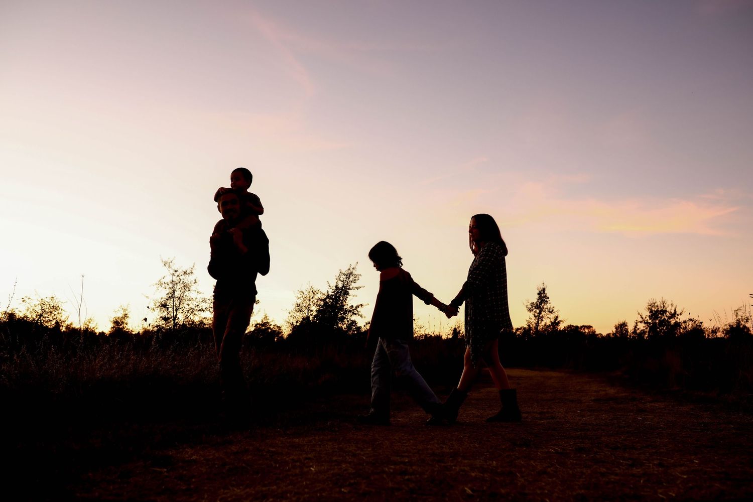 Silhouetted figures standing outdoors together against a soft pink and purple sunset sky.