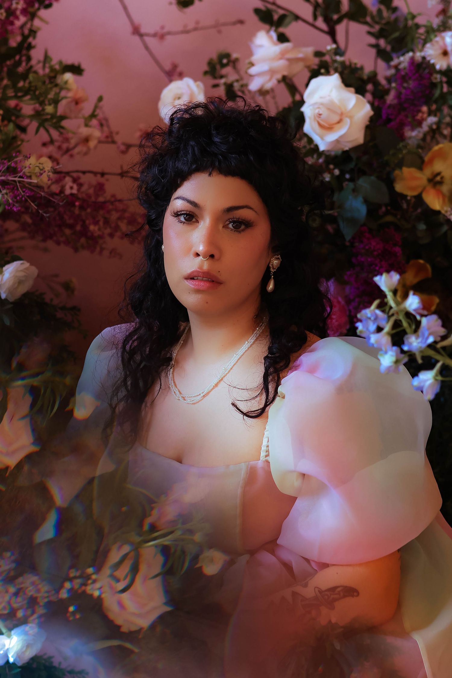 Portrait surrounded by roses featuring woman in puffy sleeve dress against pink background.