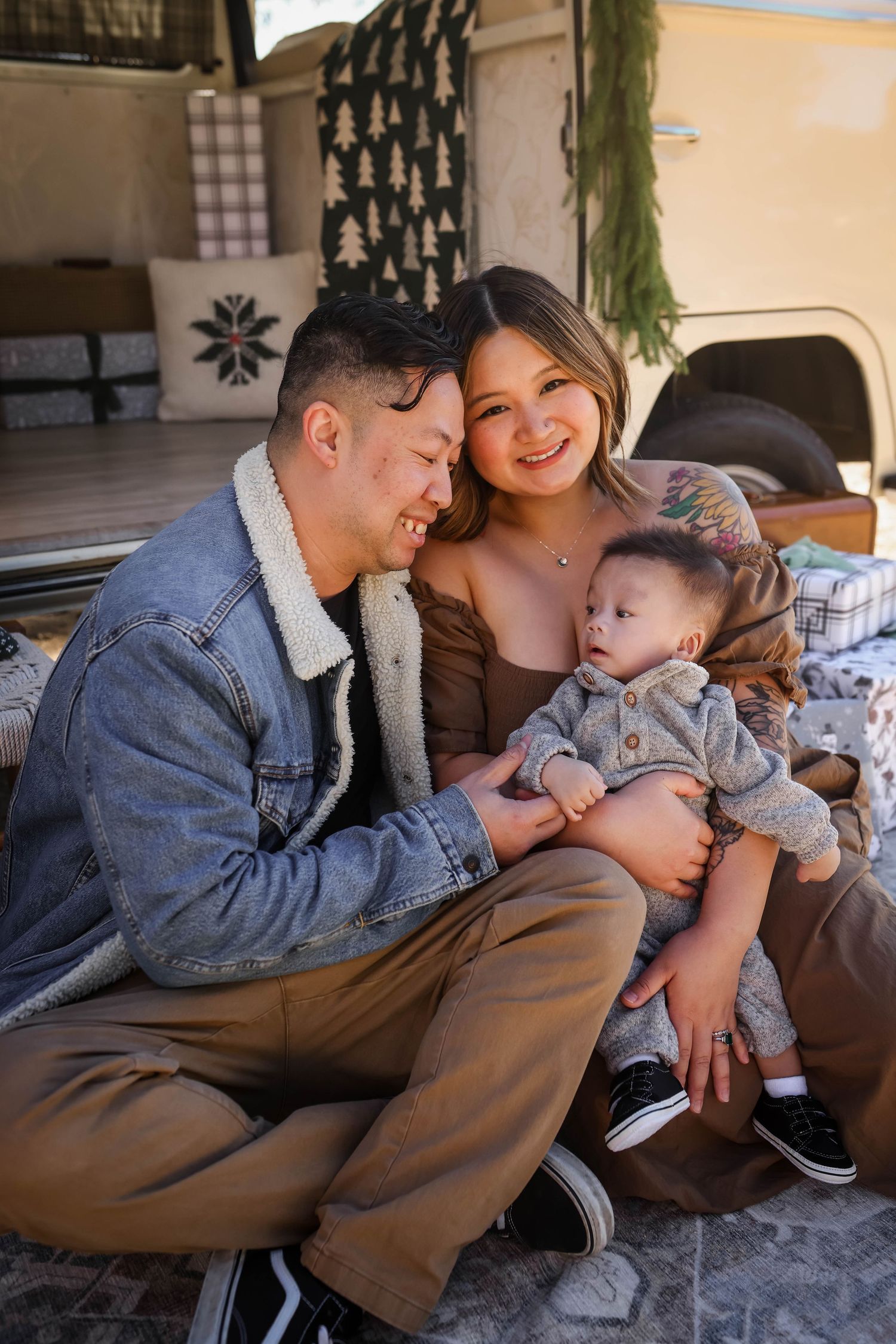 Young family sharing tender moment together in casual clothing while sitting on floor near camper van or RV for the holidays.