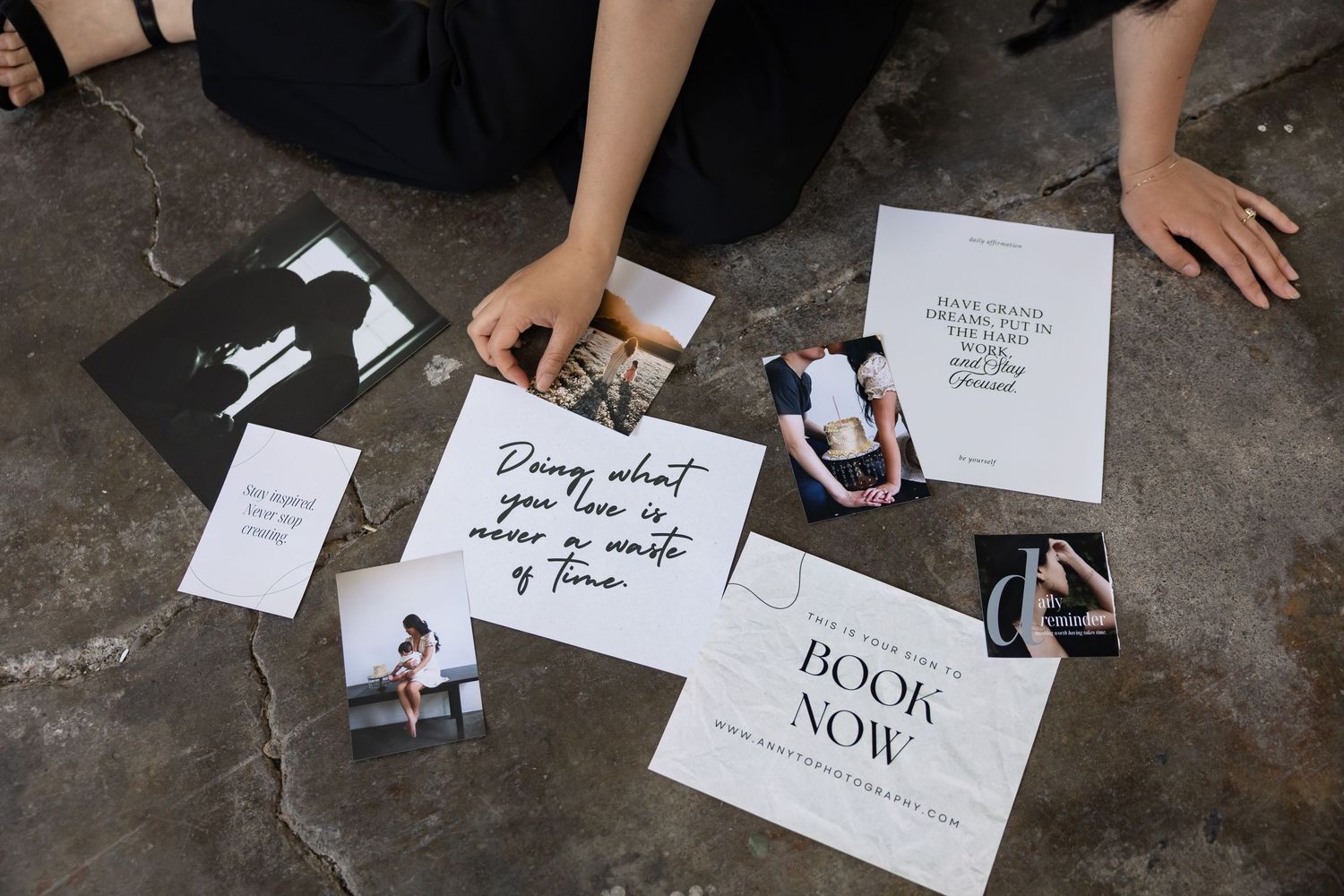 Various photographs and inspirational quote cards scattered on a concrete floor with someone's hands arranging them.