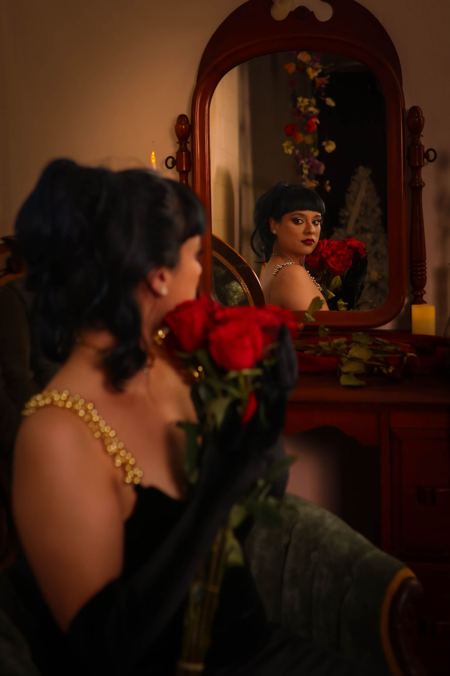 A vintage-inspired moody scene of a person in a dark setting holding a red rose by a vanity mirror.