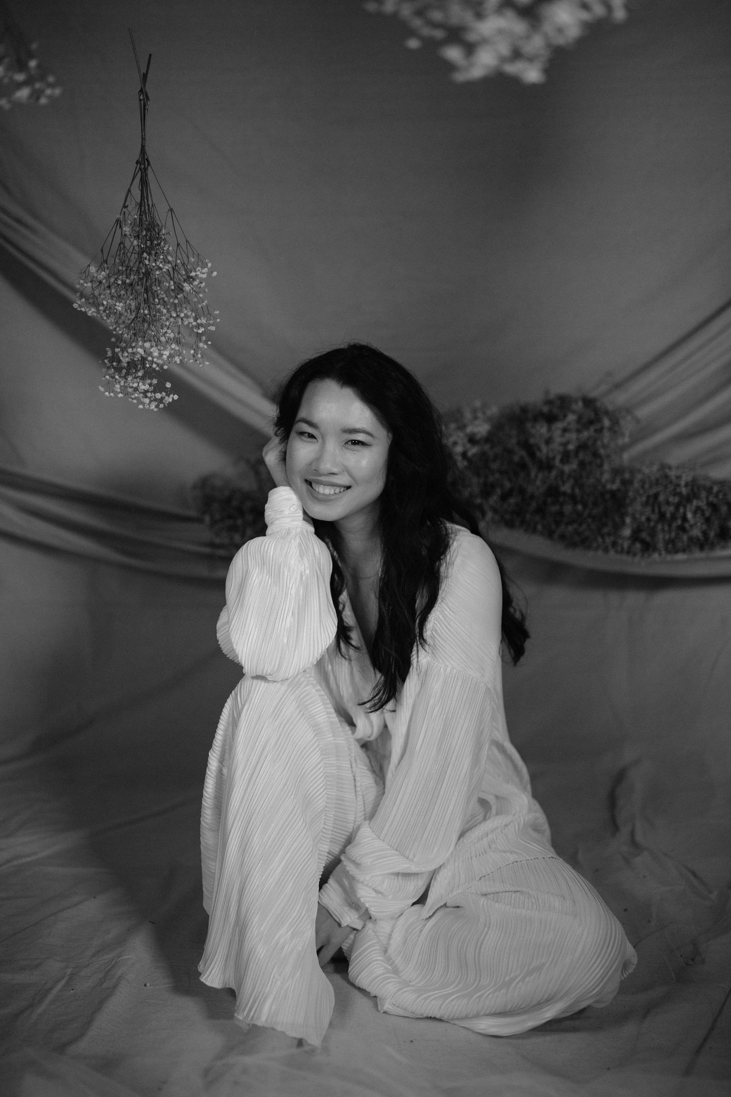 Black and white portrait of woman in flowing white outfit with hanging floral decorations.