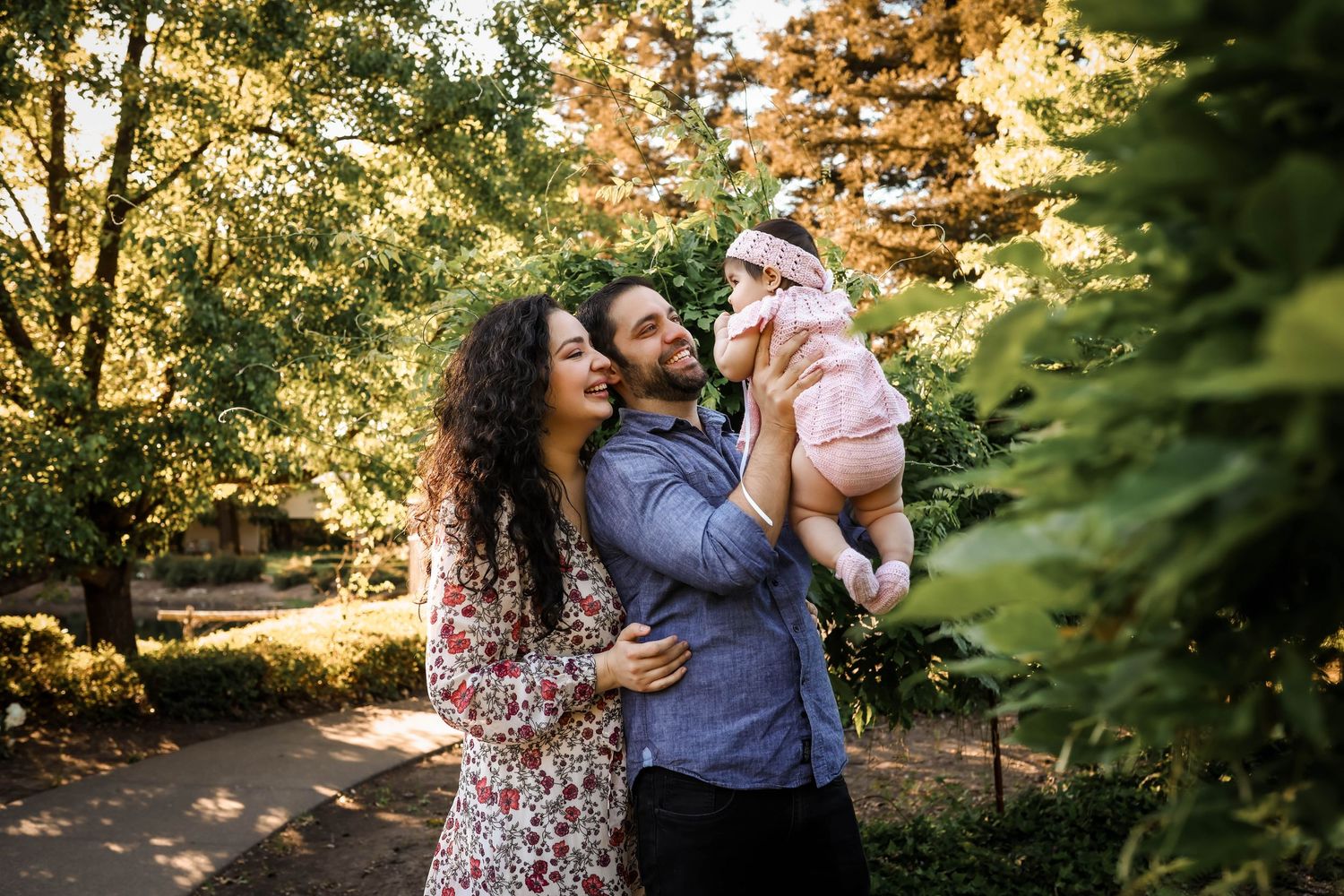 A couple and their baby share a joyful moment together outdoors surrounded by sunlit autumn foliage.