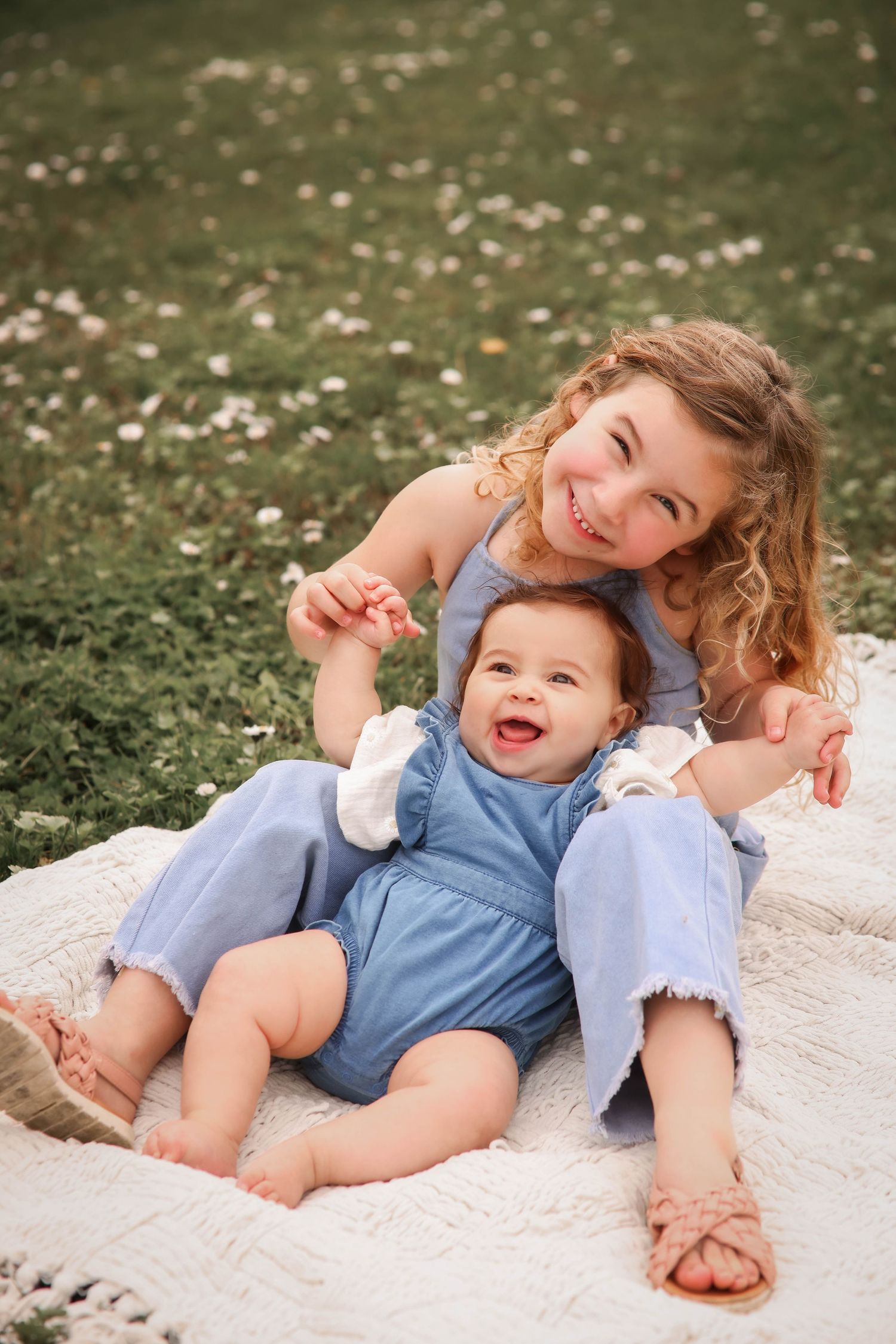 Children relaxing together on a white blanket in a grassy field with flowers.
