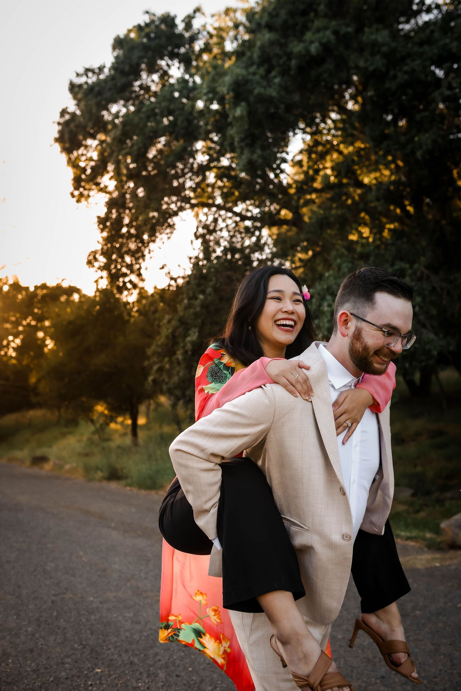 A couple shares a joyful moment at sunset on a rural path, with golden light filtering through trees.