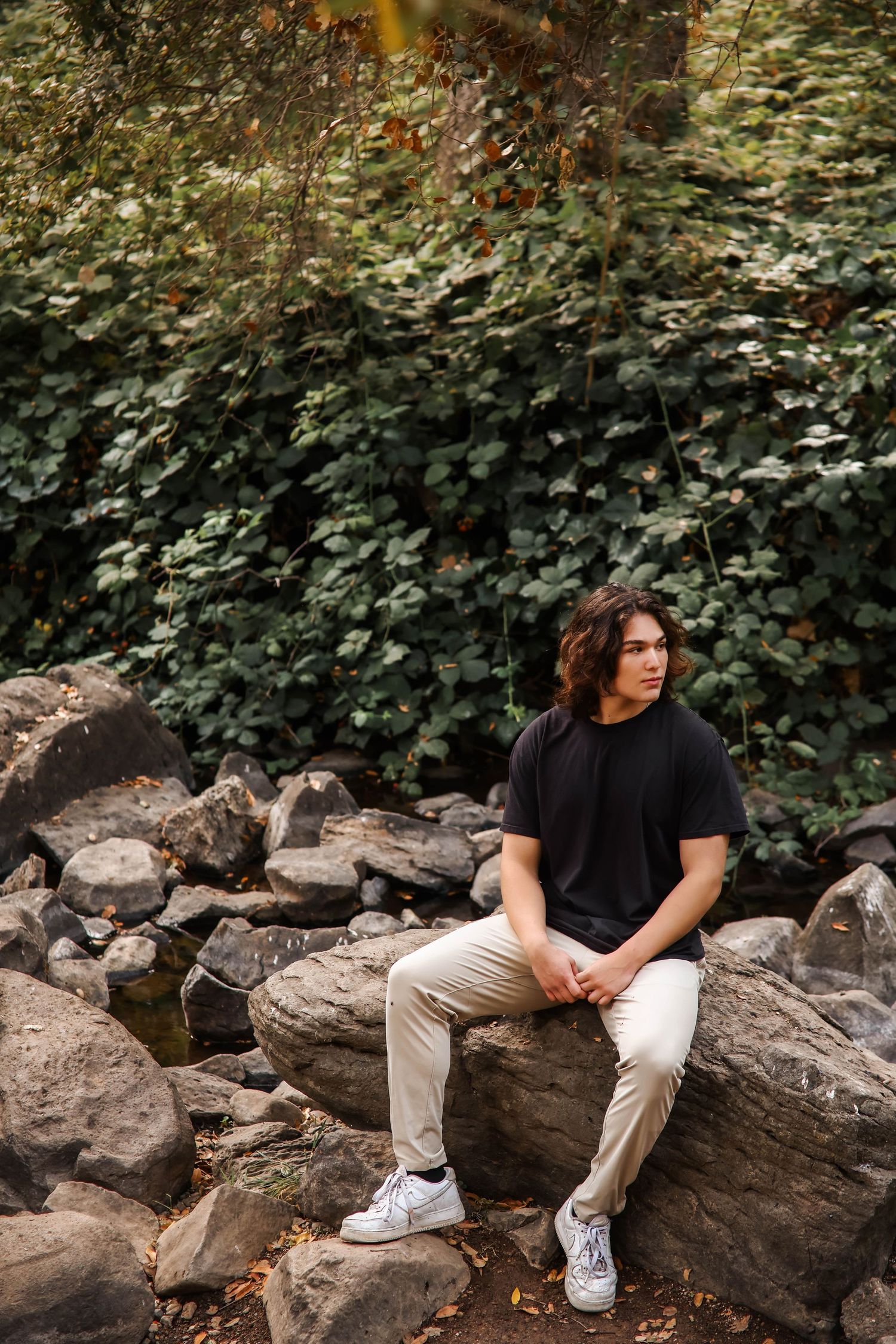 Person in casual attire sitting on rocky terrain surrounded by lush foliage.