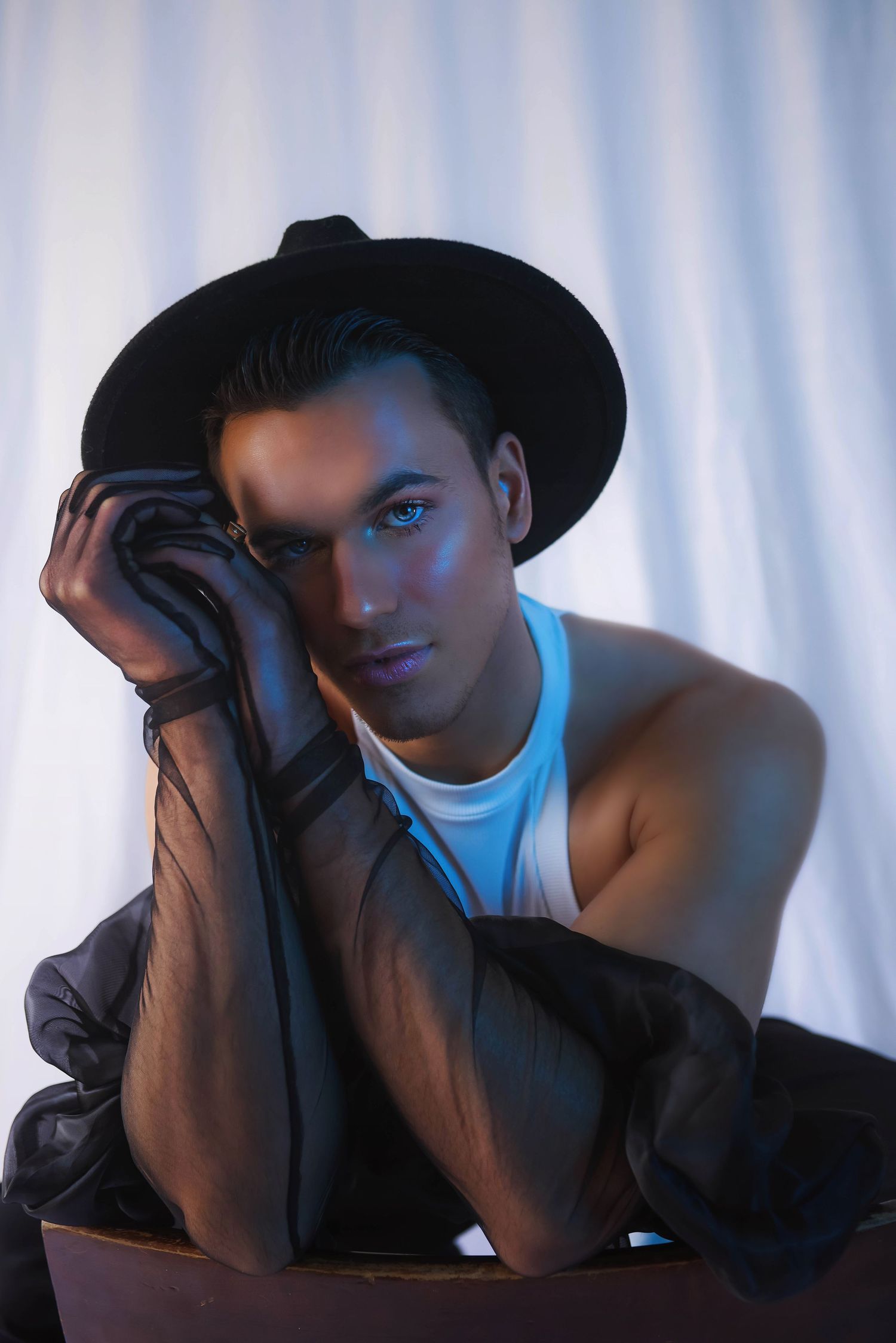 Dramatic portrait series showing a person wearing a black hat and white attire with sheer black gloves against blue lighting and white sheet