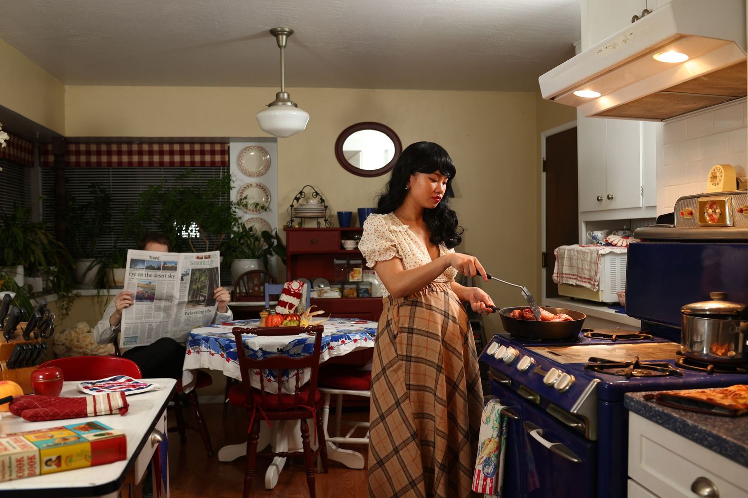 A person cooks in a cozy kitchen with plaid wallpaper border and natural wood accents. Maternity. Halloween. Vintage.