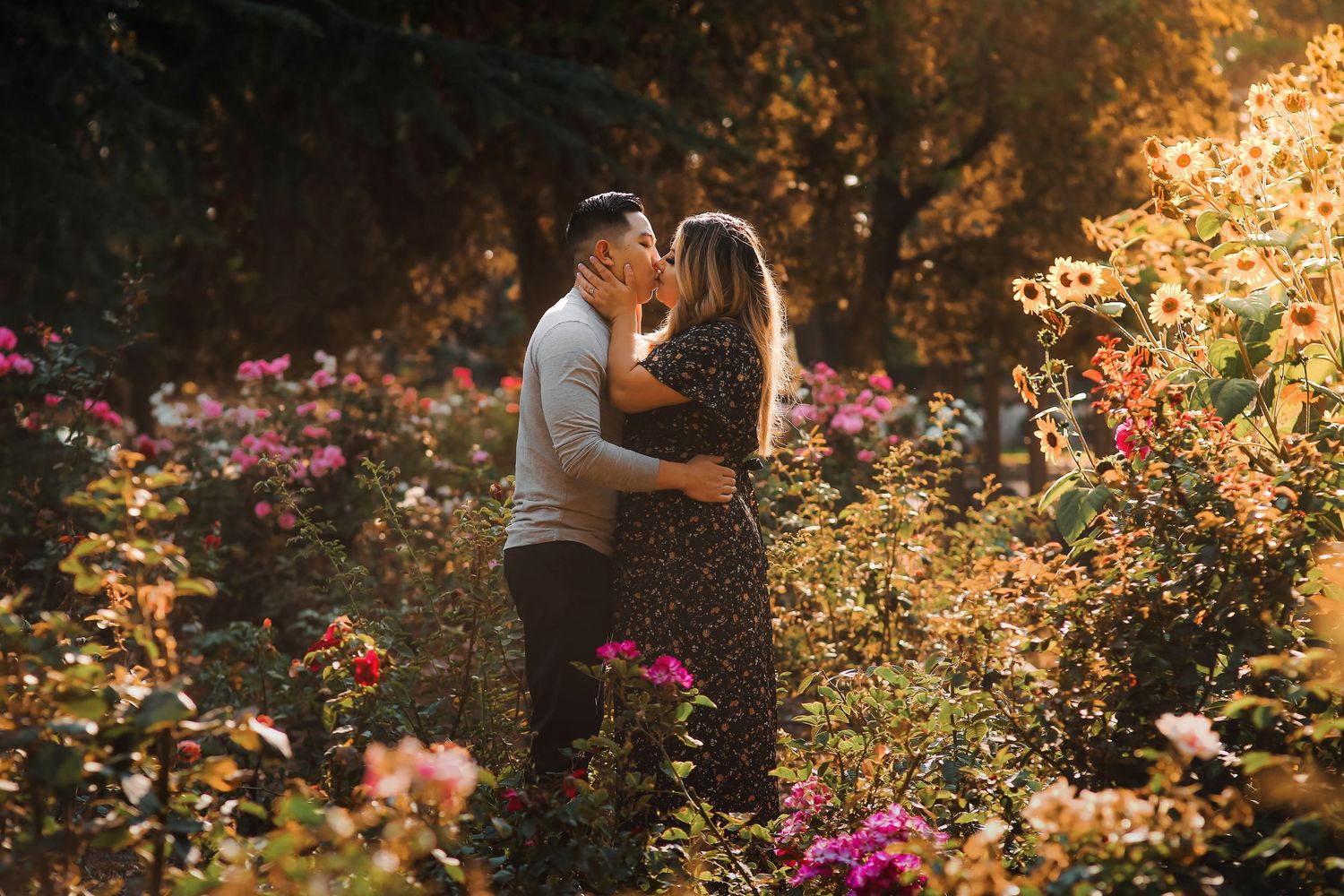 A romantic couple embraces in a garden surrounded by colorful flowers during golden hour sunset.