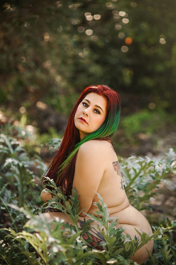 Artistic portrait in nature featuring long red and green ombre hair against a blurred bokeh background.