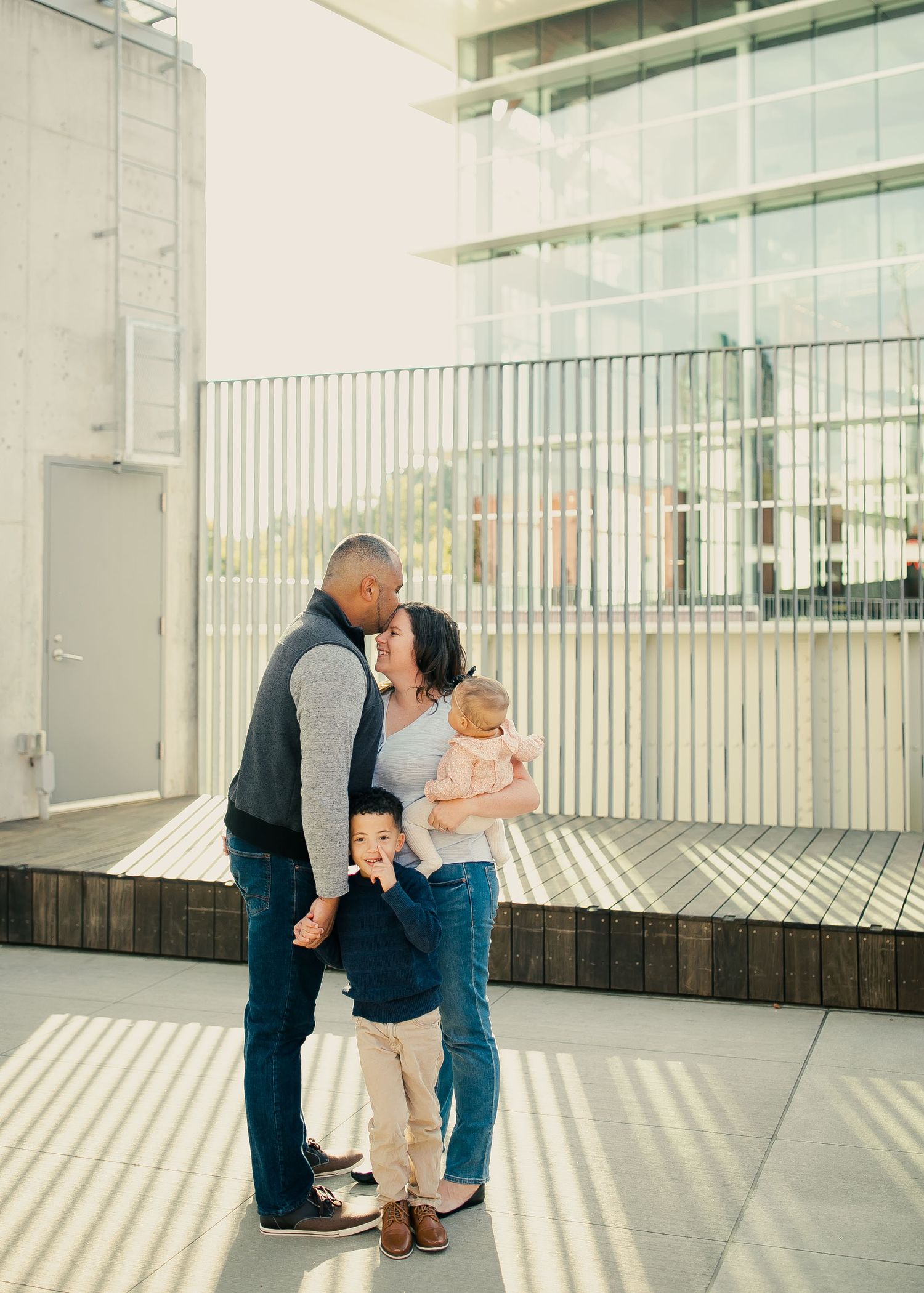 A family shares an intimate moment in a modern architectural space with dramatic shadows and natural light.