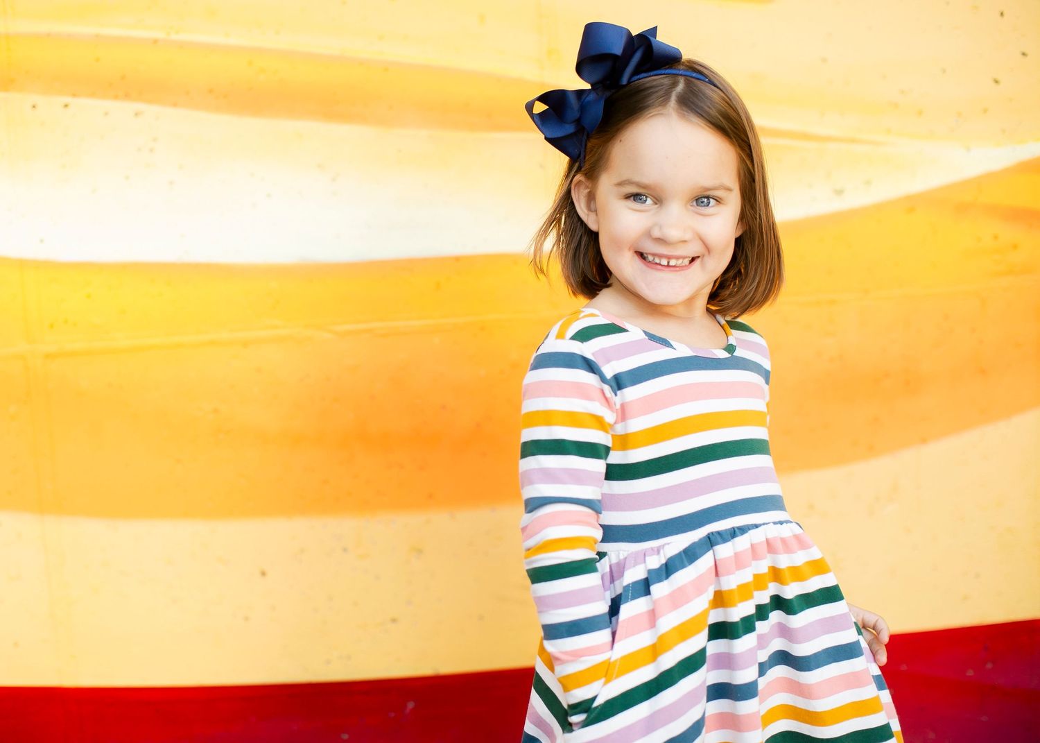 A rainbow striped sweater worn in a warm orange-lit room creates a cheerful and colorful fashion moment.