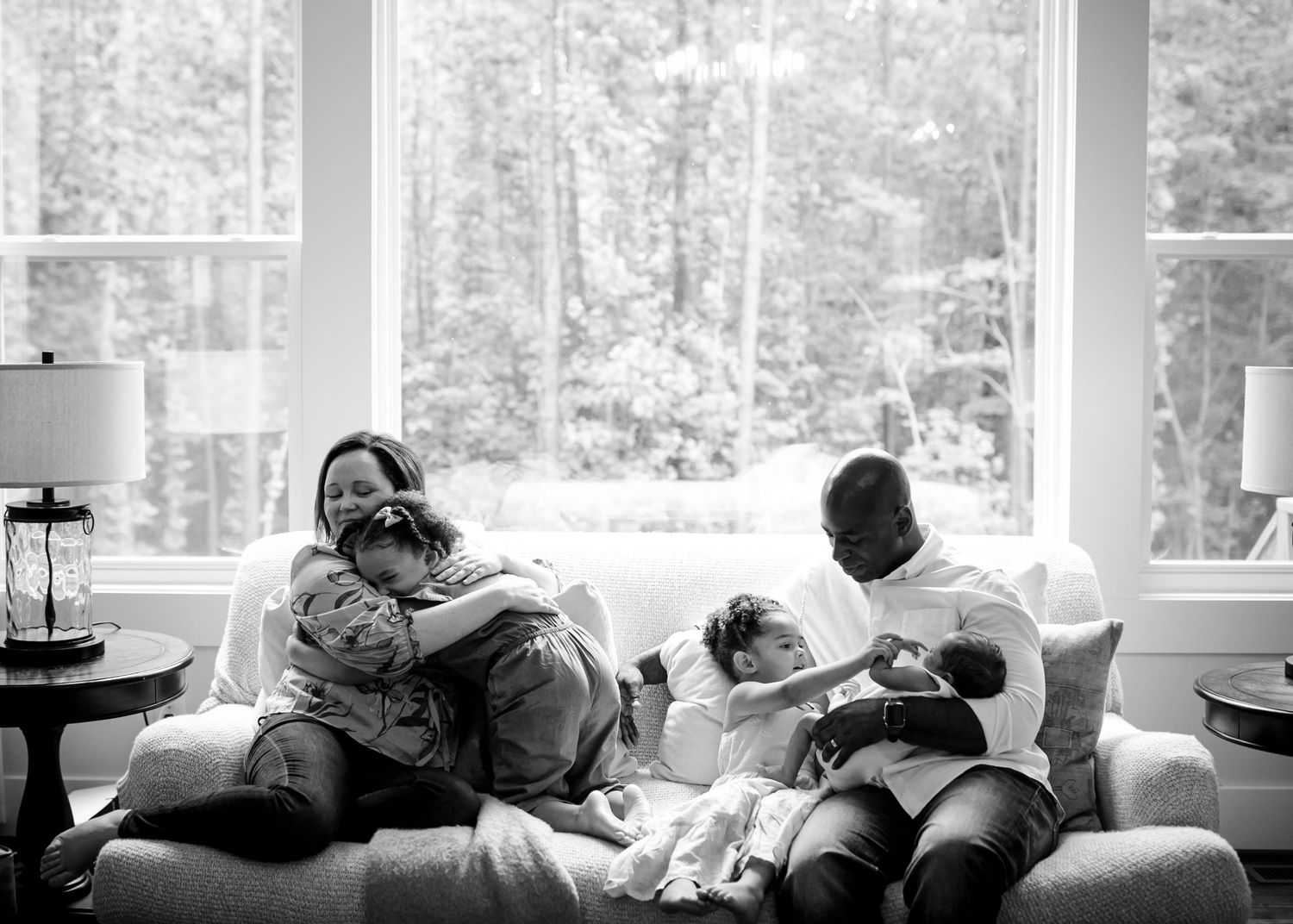A black and white photo showing people resting on a couch in a bright sunlit room.