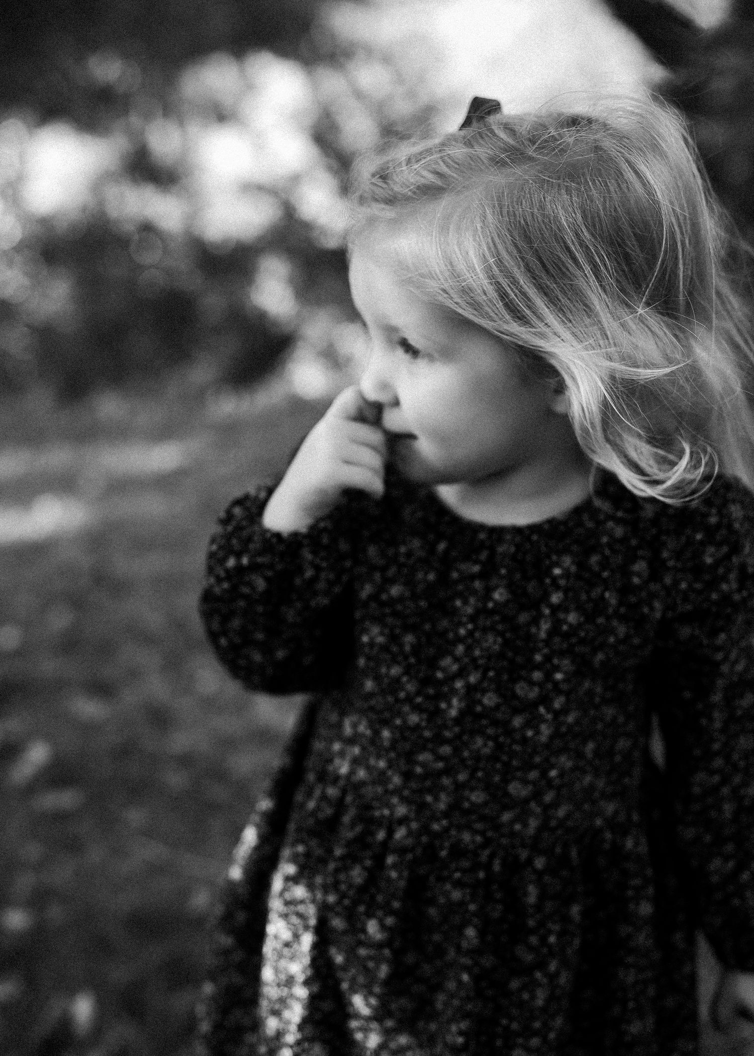 A black and white photograph of a child in a black dress with white accents looking to the side.
