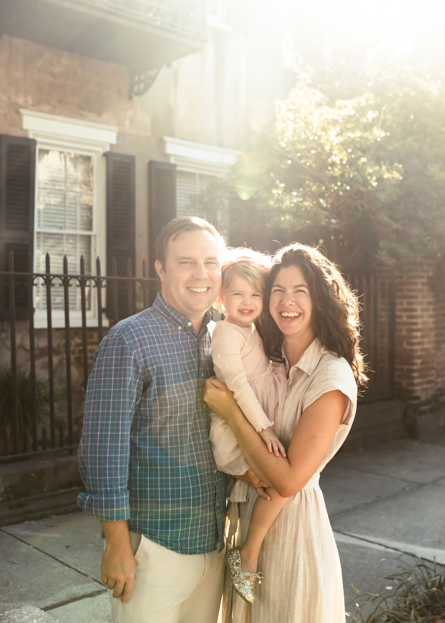 A family shares a happy moment together during golden hour. The sun is creating a slight flare at the top of the image.