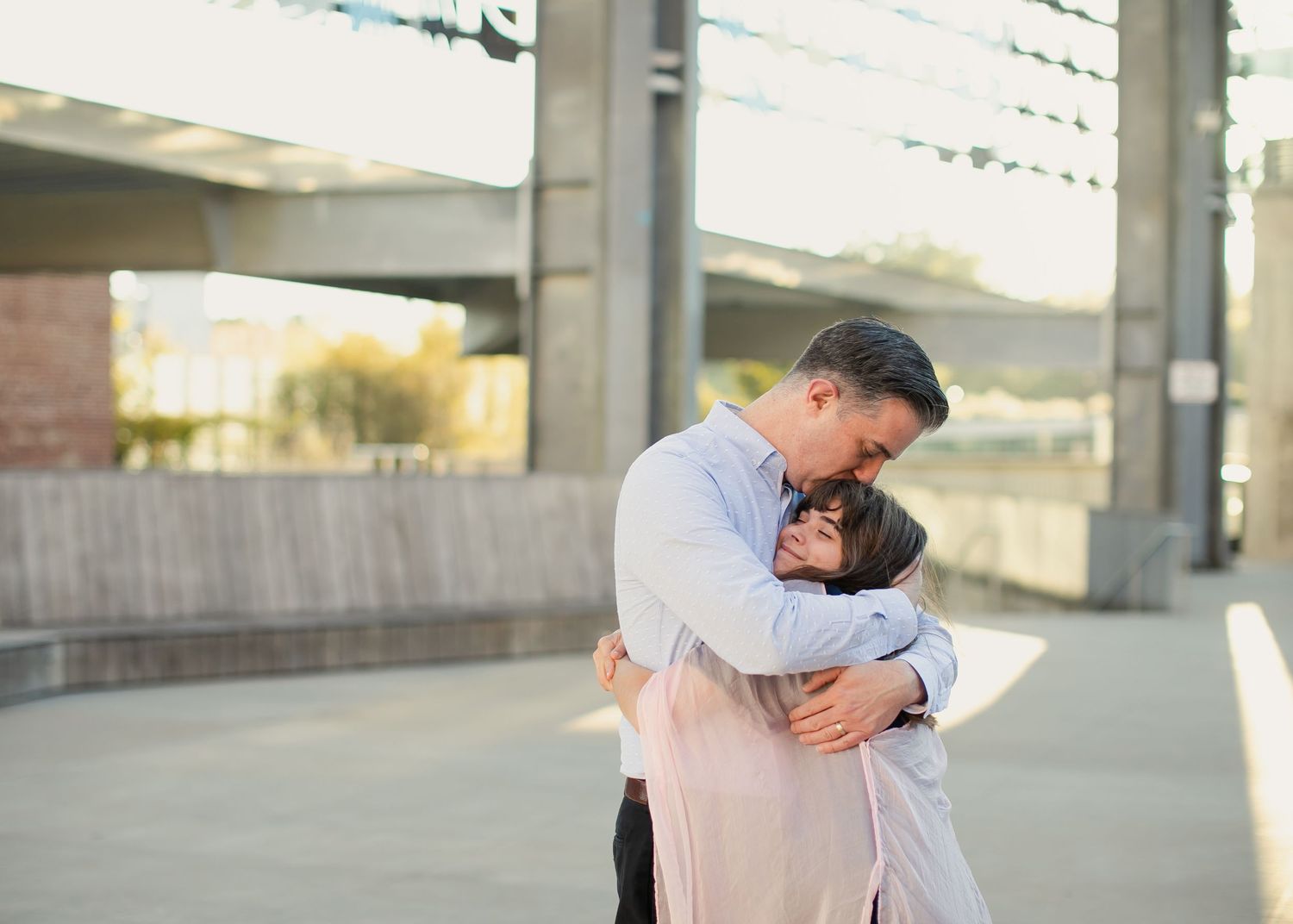 Two people share an embrace while standing on a concrete walkway during golden hour.