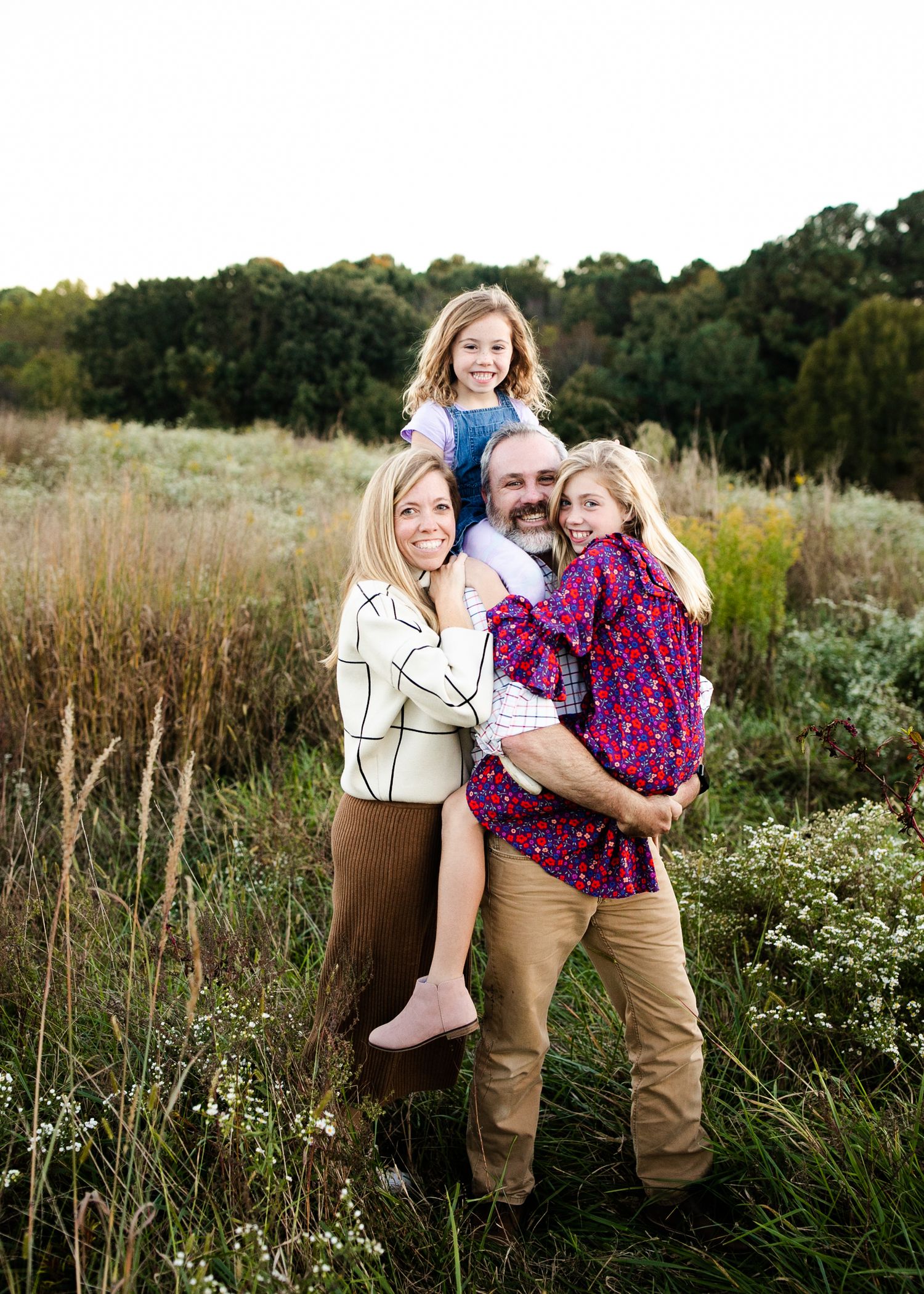 A family poses together in a field of tall grass during golden hour with trees in the background.