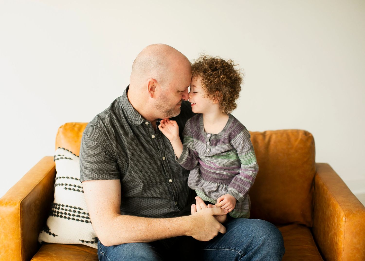 Parent and child share a tender moment while sitting together on a brown leather couch.