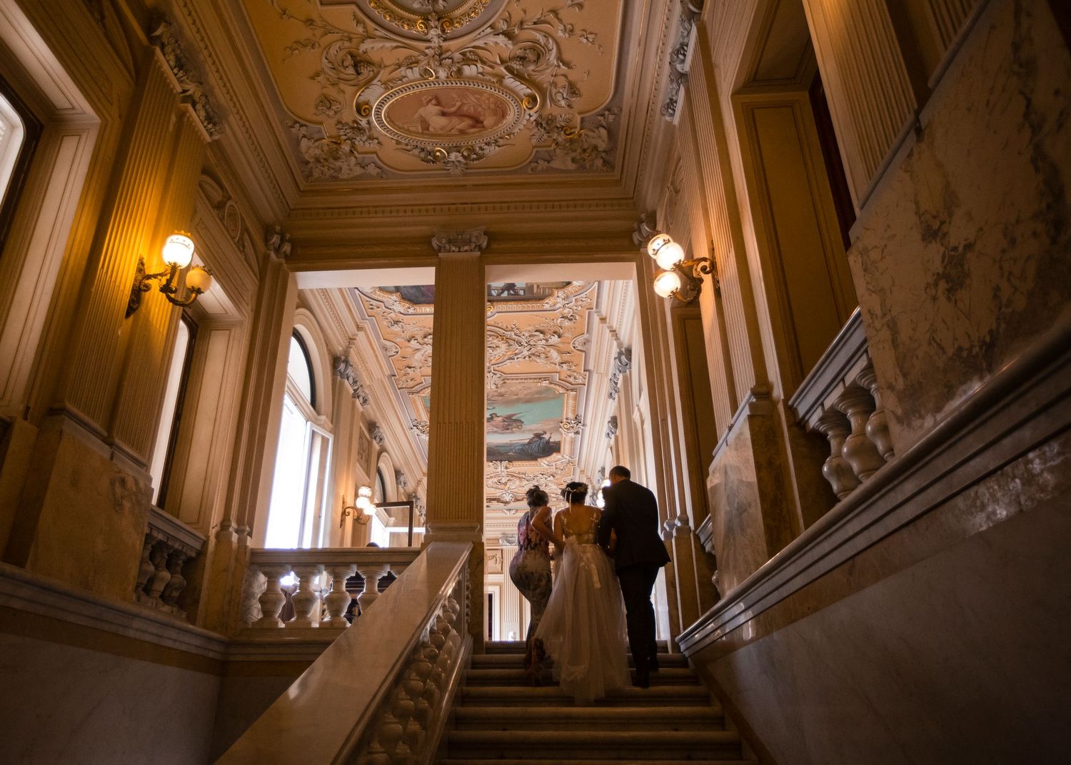 A bride prepares to enter the main room of a palace surrounded on both sides by her parents before the start of the wedding ceremony.