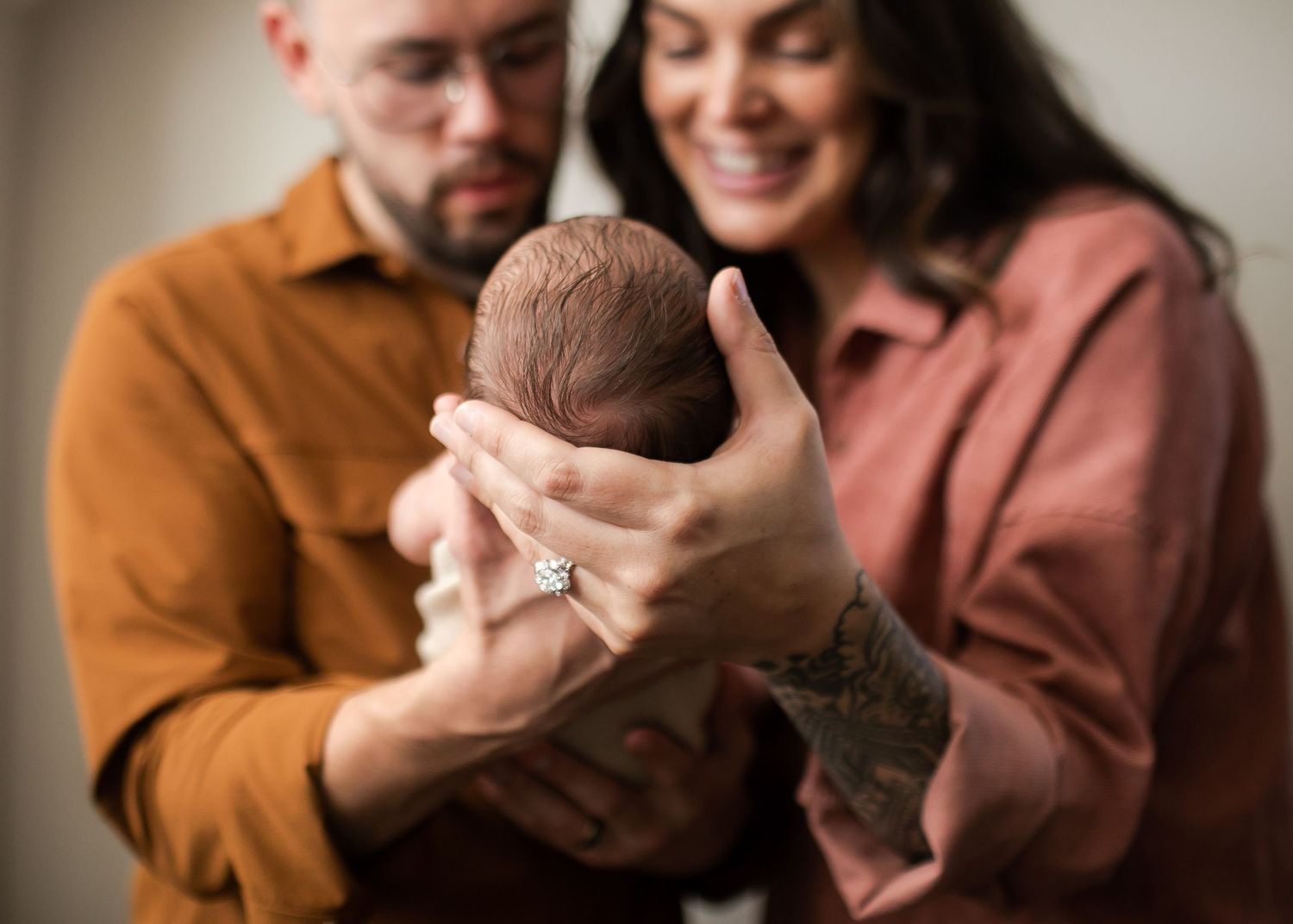 Two people in brown and pink clothing hold a newborn together in their outstretched arms.