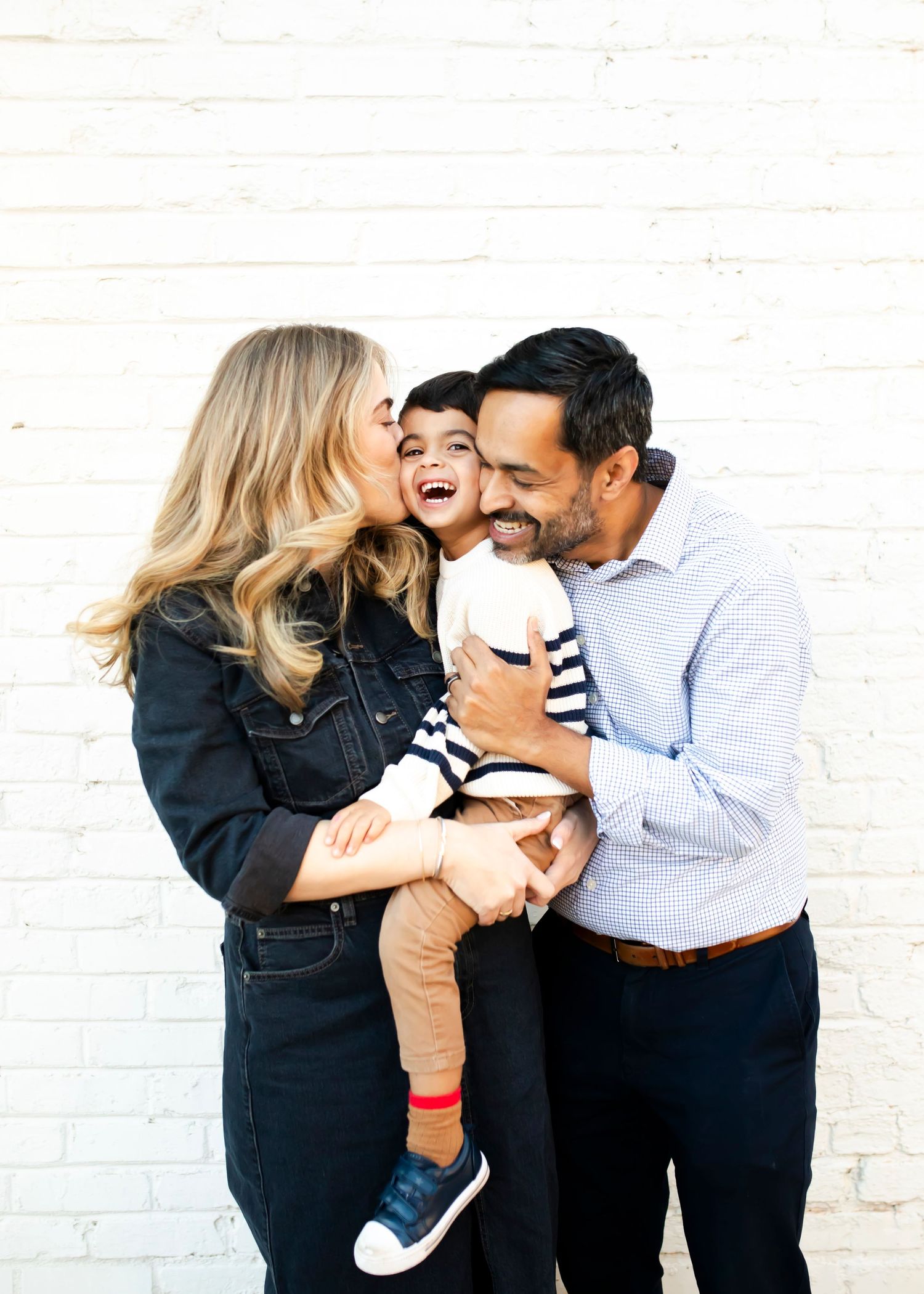 A family shares a blisfull moment together against a white brick wall.