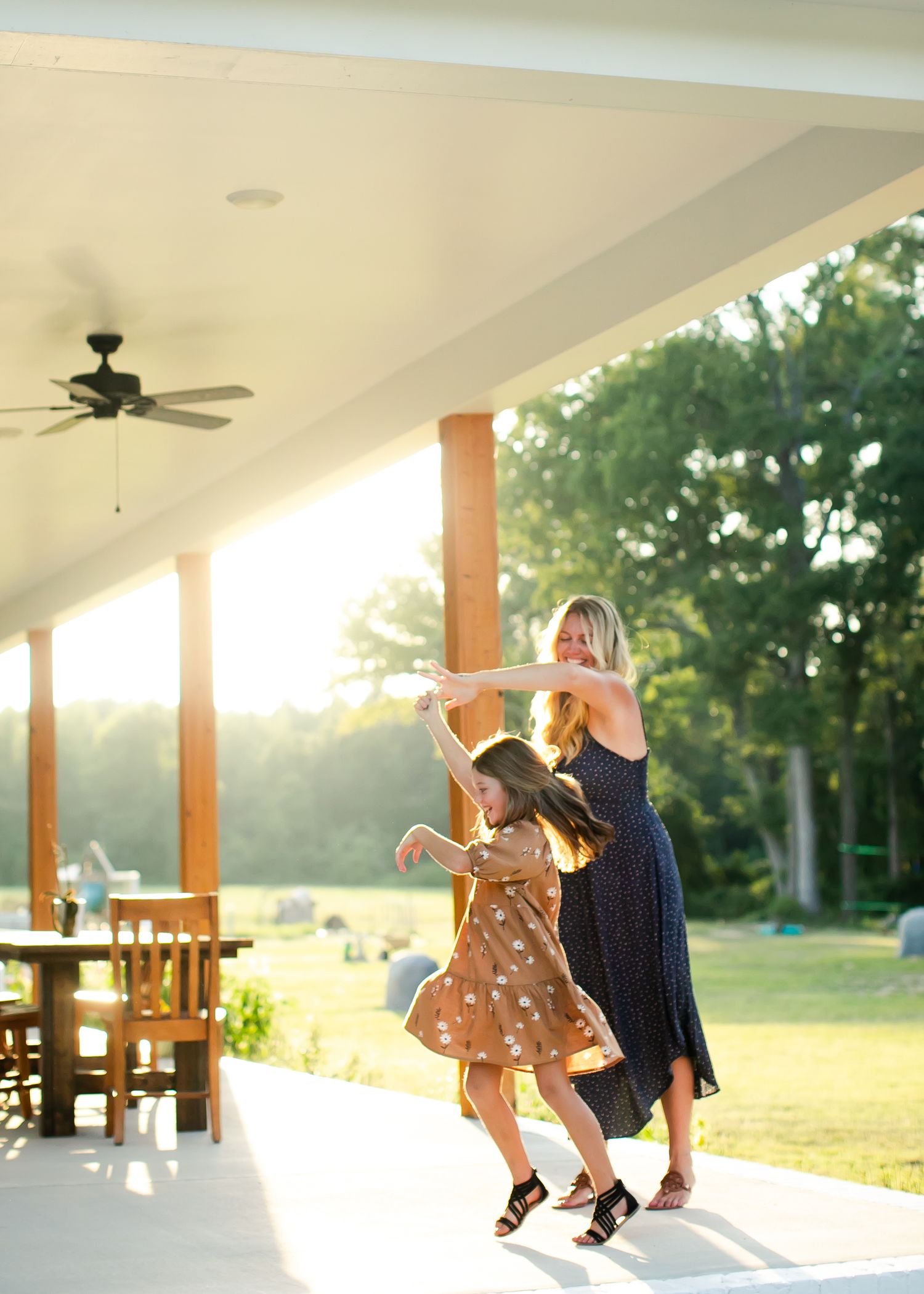 An adult and child dance together on a porch at sunset, creating a silhouette against the golden light.