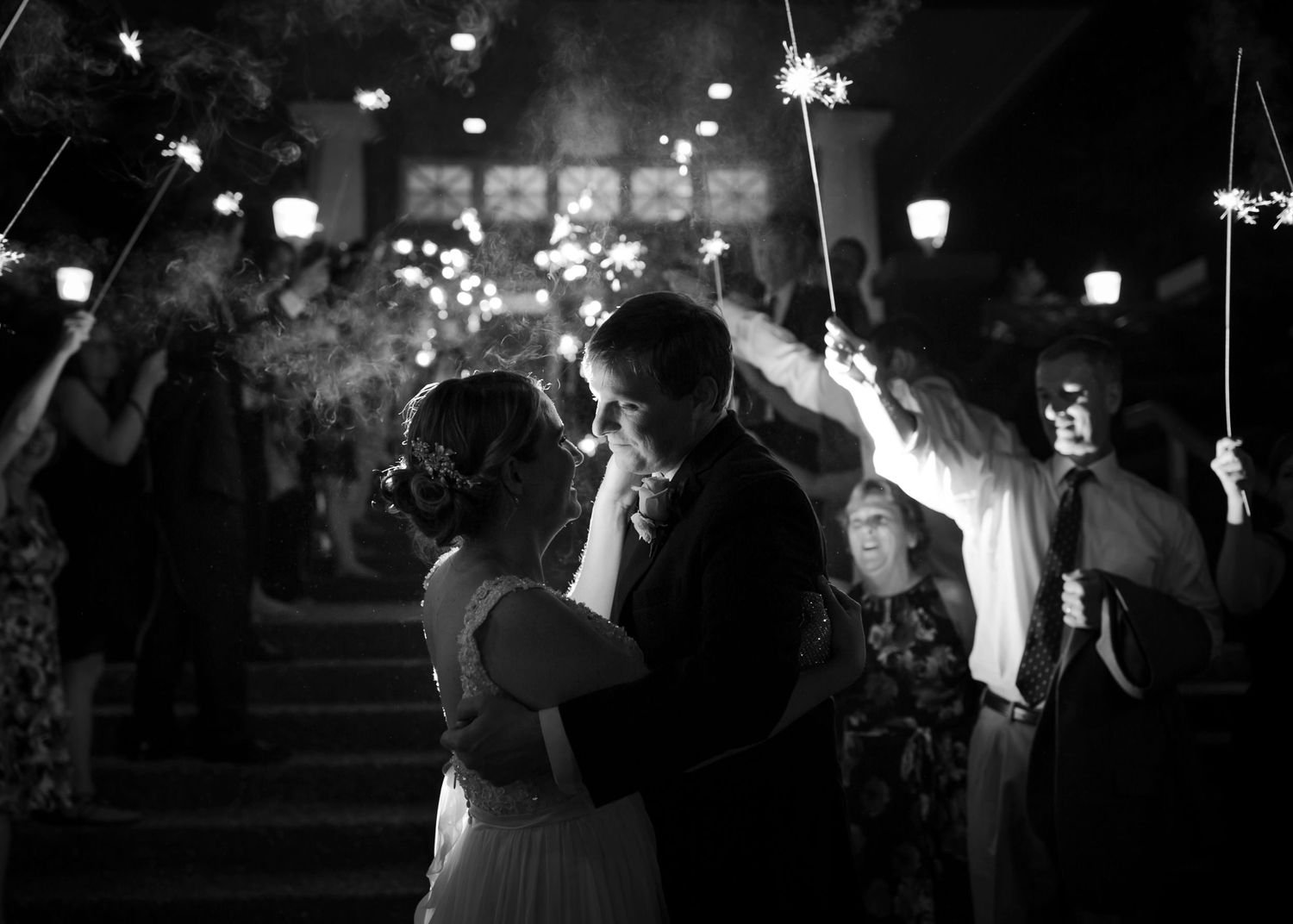 A romantic couple dances together under twinkling lights at an outdoor evening celebration.