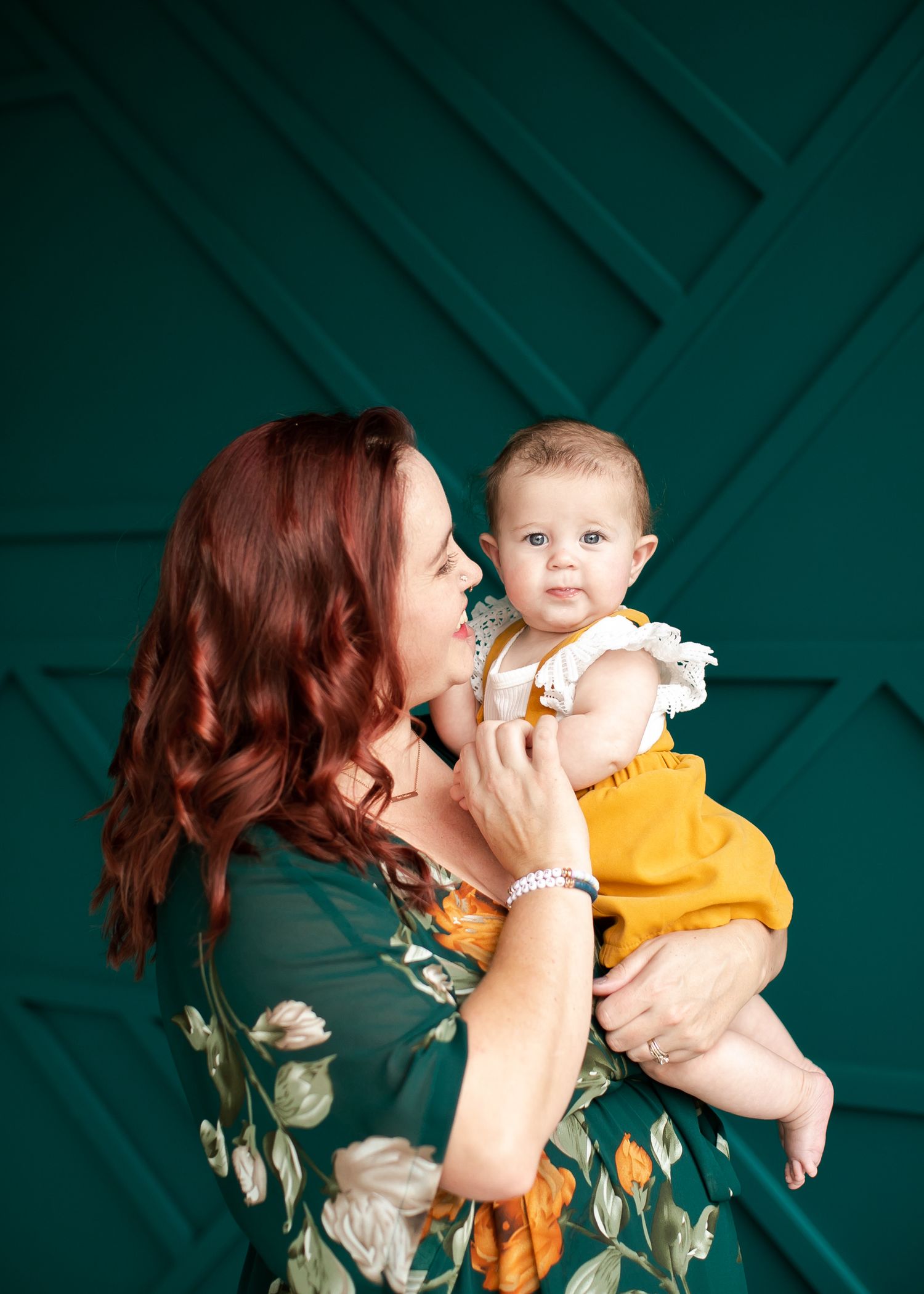A tender moment between parent and baby in coordinating green and yellow outfits against a teal geometric backdrop.