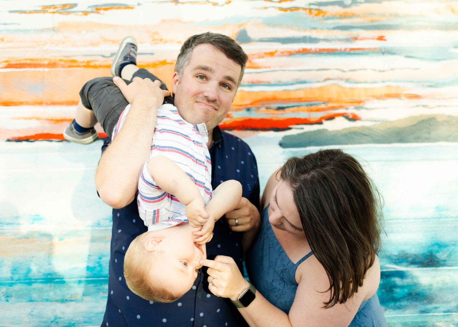 A family plays together against a colorful watercolor background with teal and orange tones.