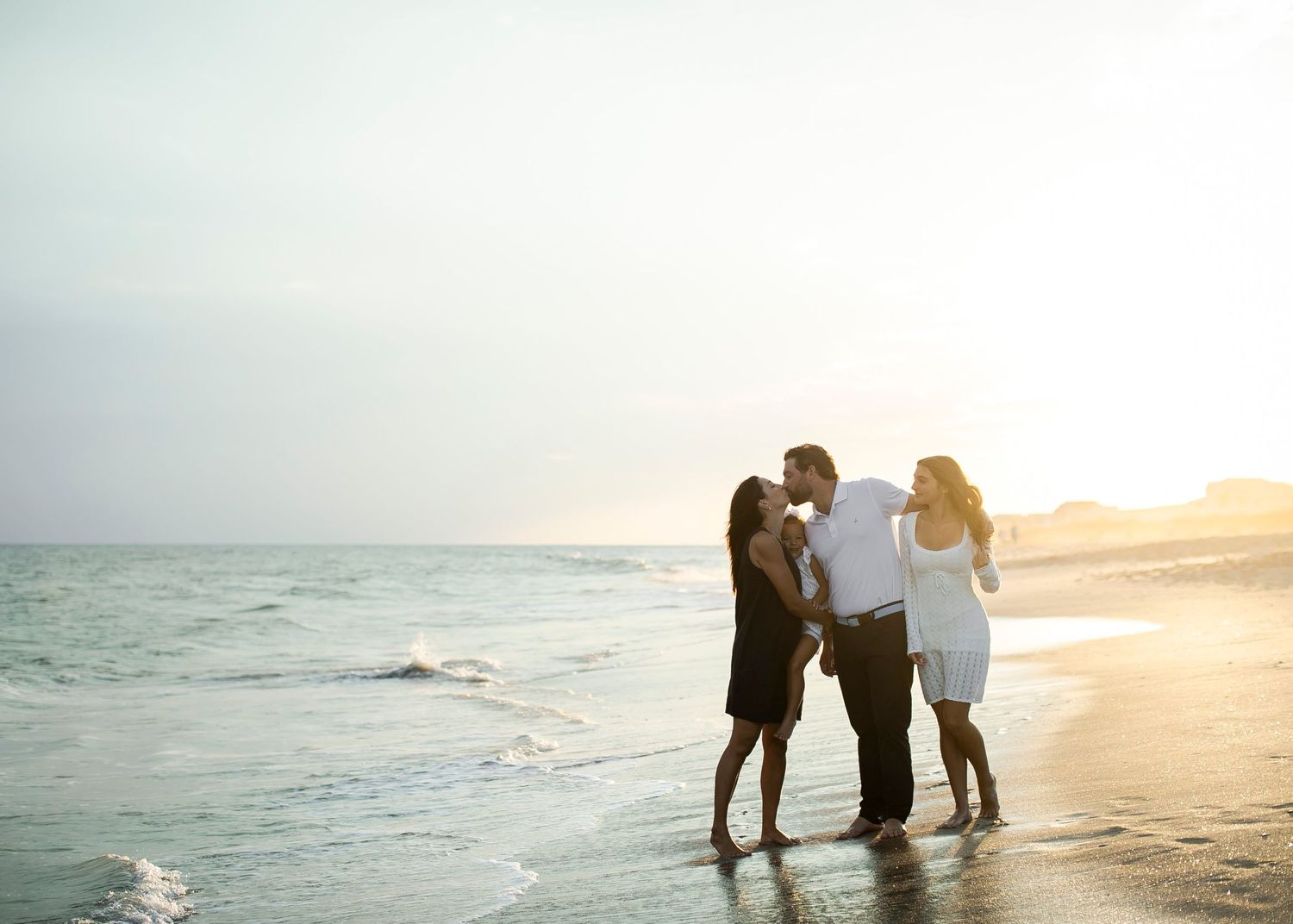 Silhouetted figures walk along a misty beach shoreline at sunset with waves gently rolling in.