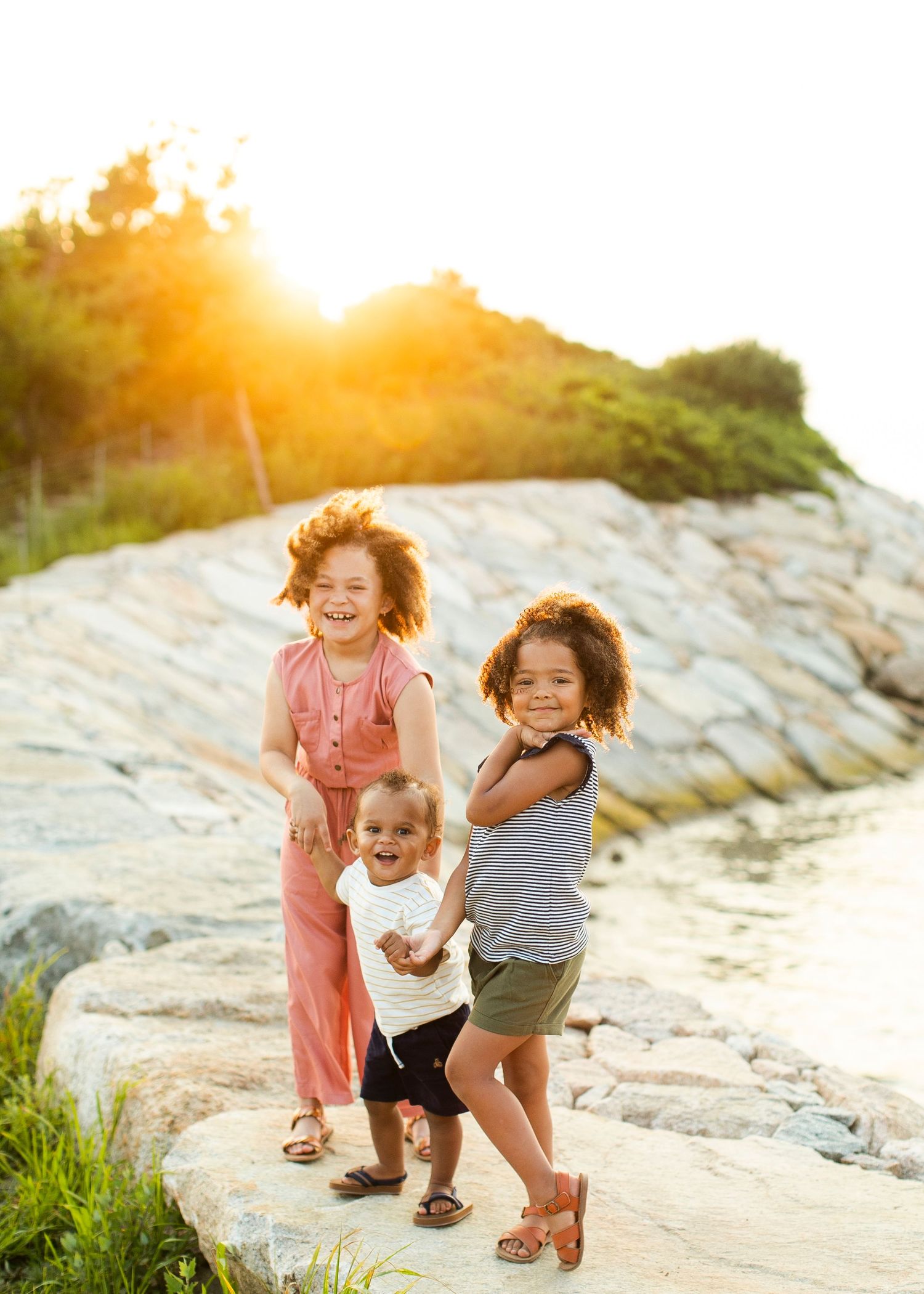 Children standing together on rocky terrain during golden hour sunset at the beach.