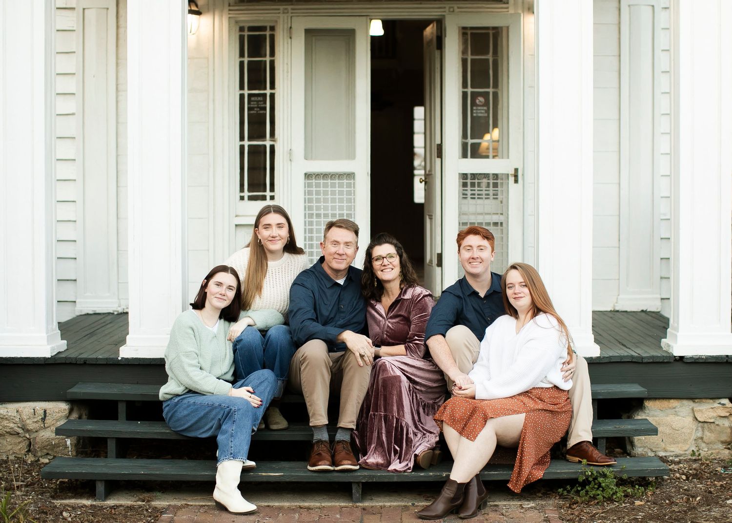 A family sits together on the black steps of a white house.