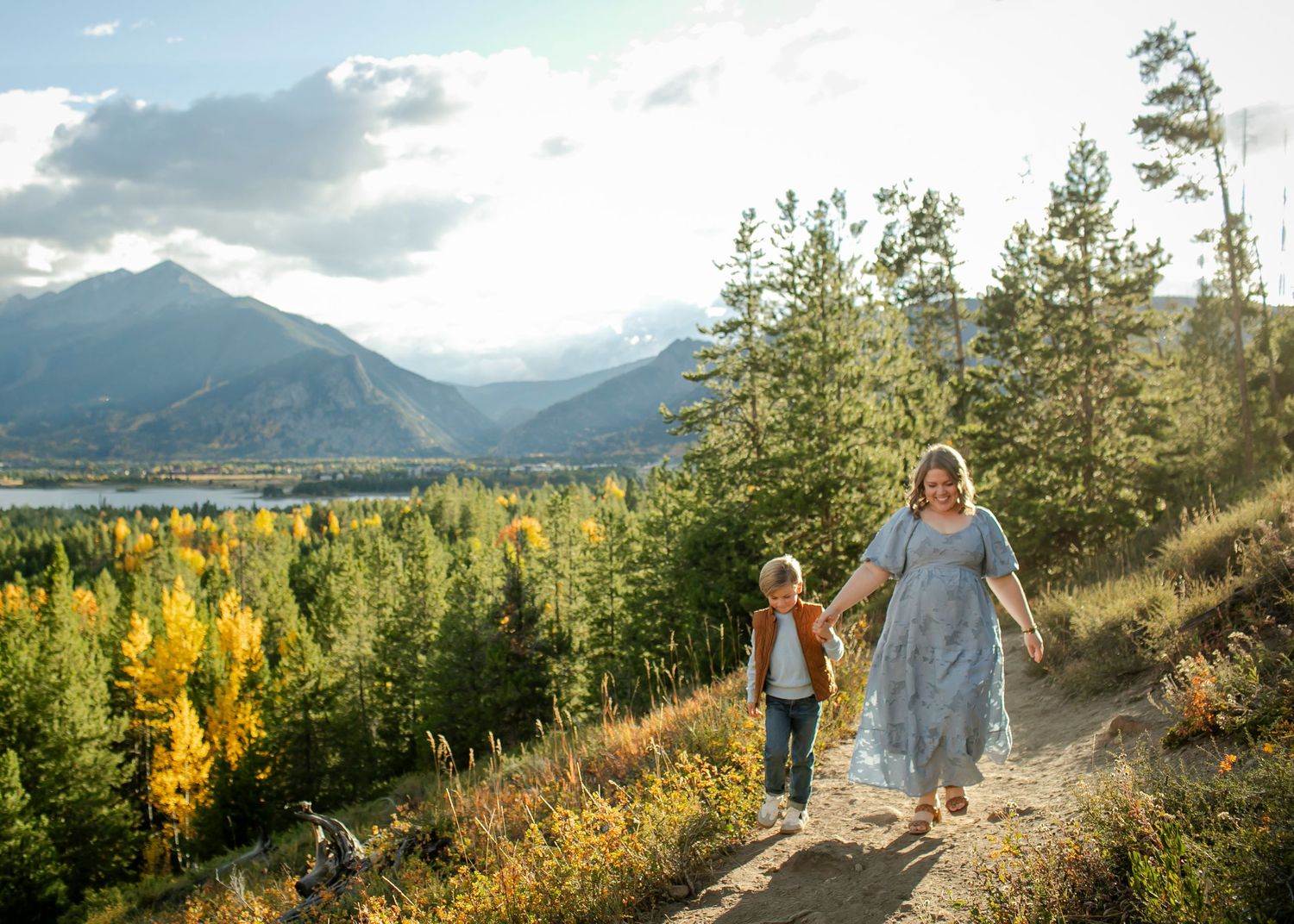 People hiking on mountain trail overlooking scenic lake and autumn foliage in mountain landscape.