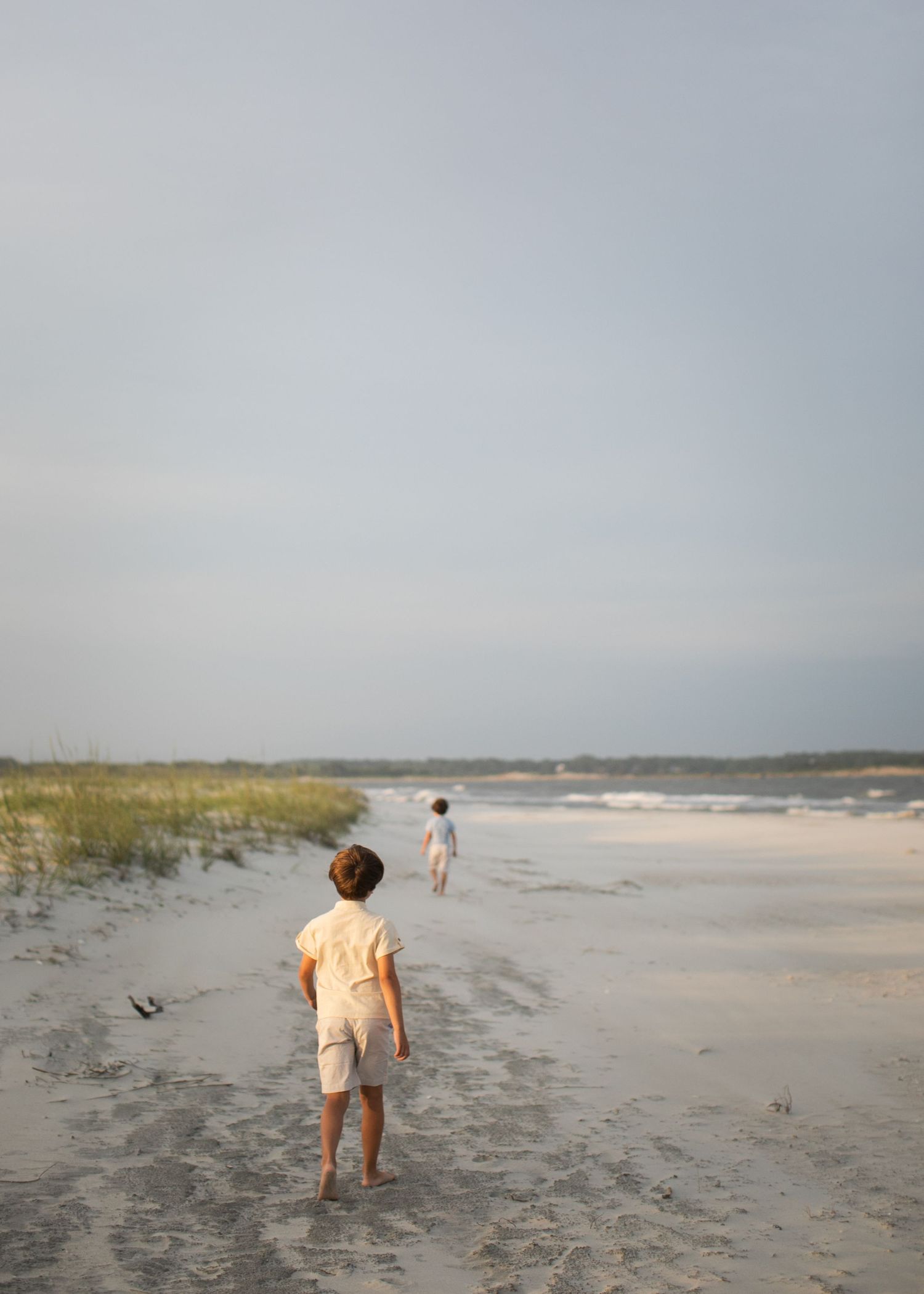 Two children walking on a beach with waves crashing agains the shoreline.