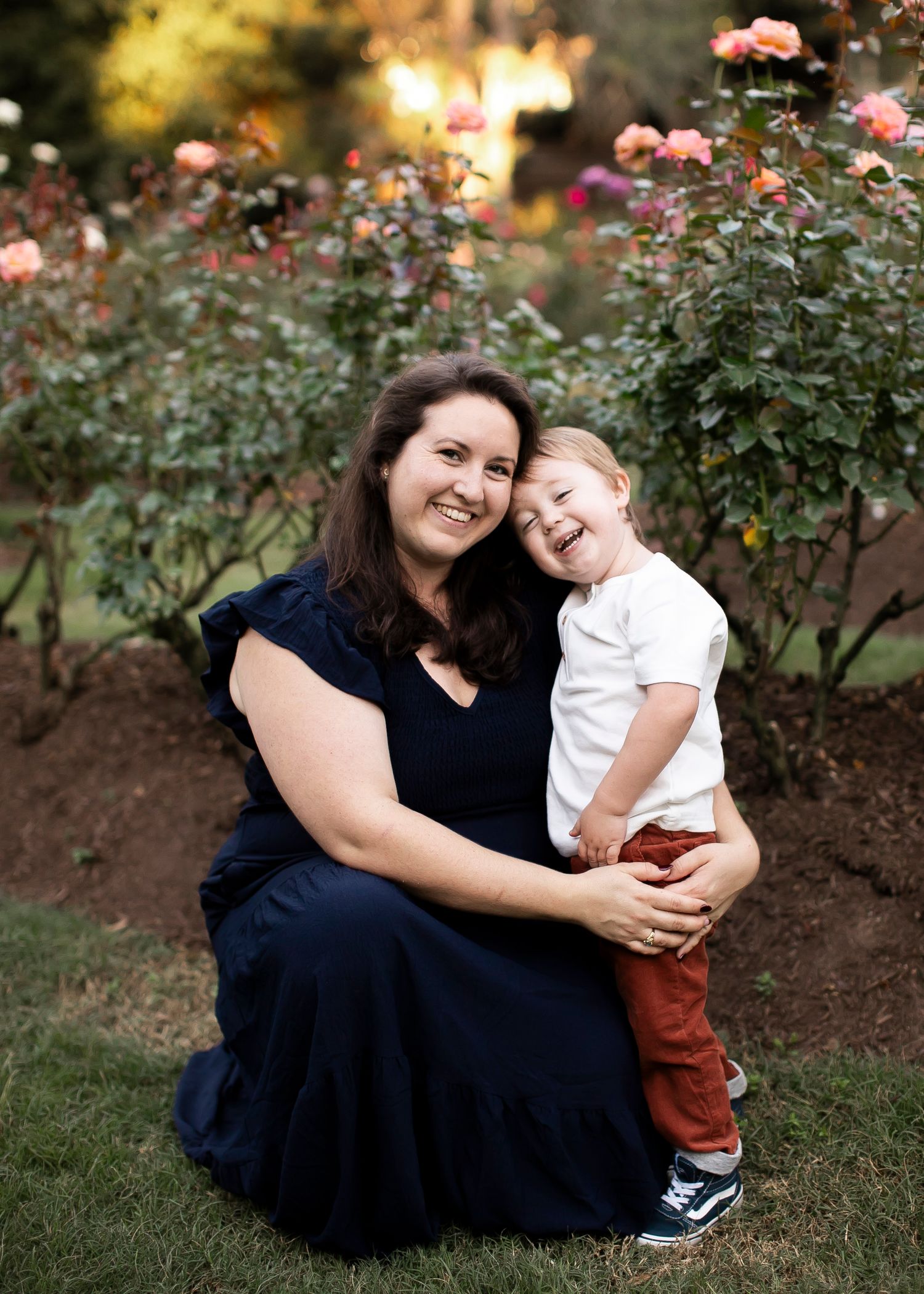 A tender moment captured in a rose garden at sunset with blooming pink flowers in the background.