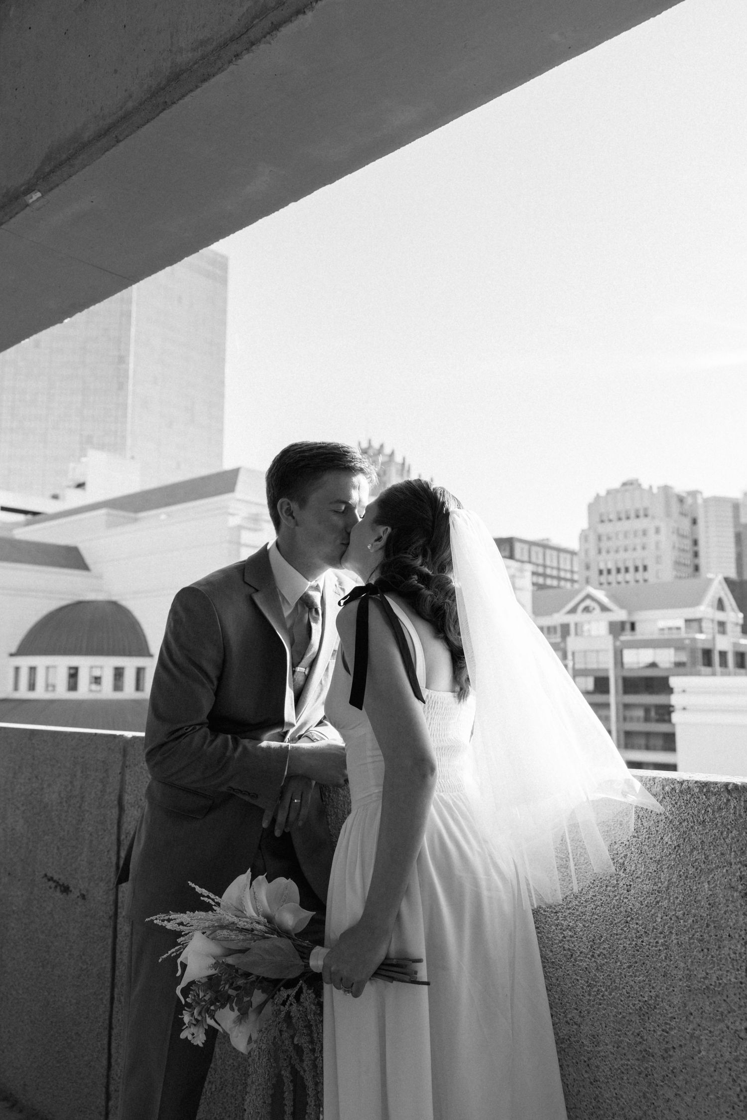 Bride and groom sharing a kiss on rooftop with city skyline in black and white wedding photo.