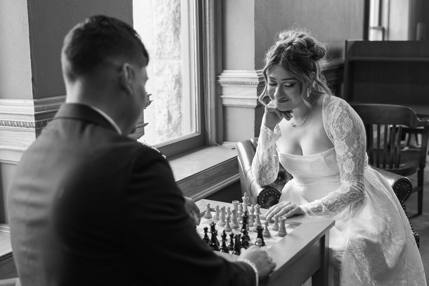 Black and white photo of bride and groom playing chess together on their wedding day.