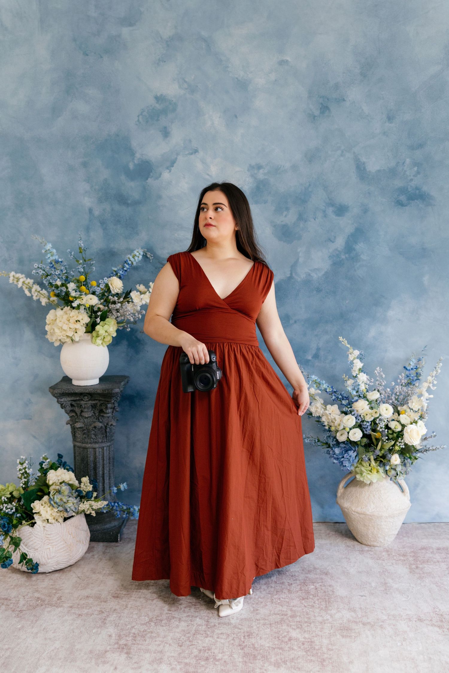 A rustic photo series featuring a flowy rust-colored dress against a moody blue backdrop with white floral arrangements.