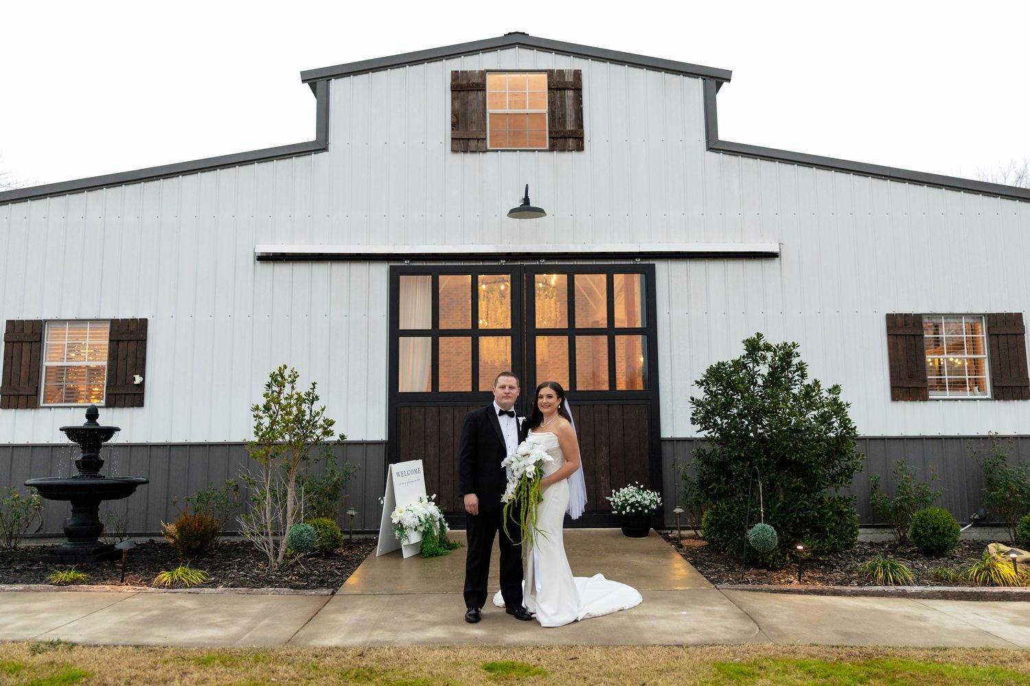 A panoramic view of a white barn wedding venue with elegant black shutters and landscaping details.